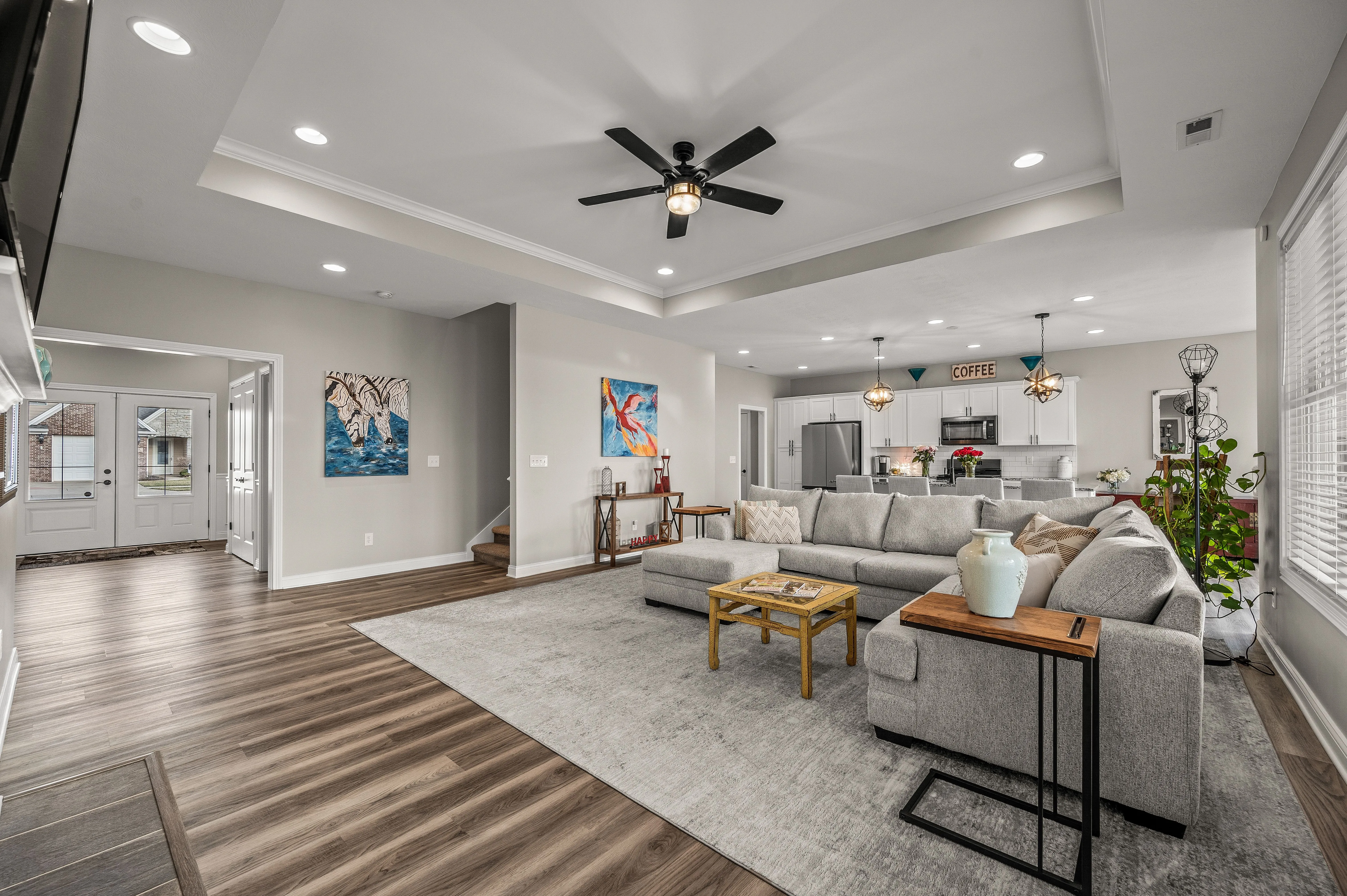 Spacious modern living room seamlessly transitioning into kitchen area with contemporary furniture and decor, hardwood flooring, and ample natural light.