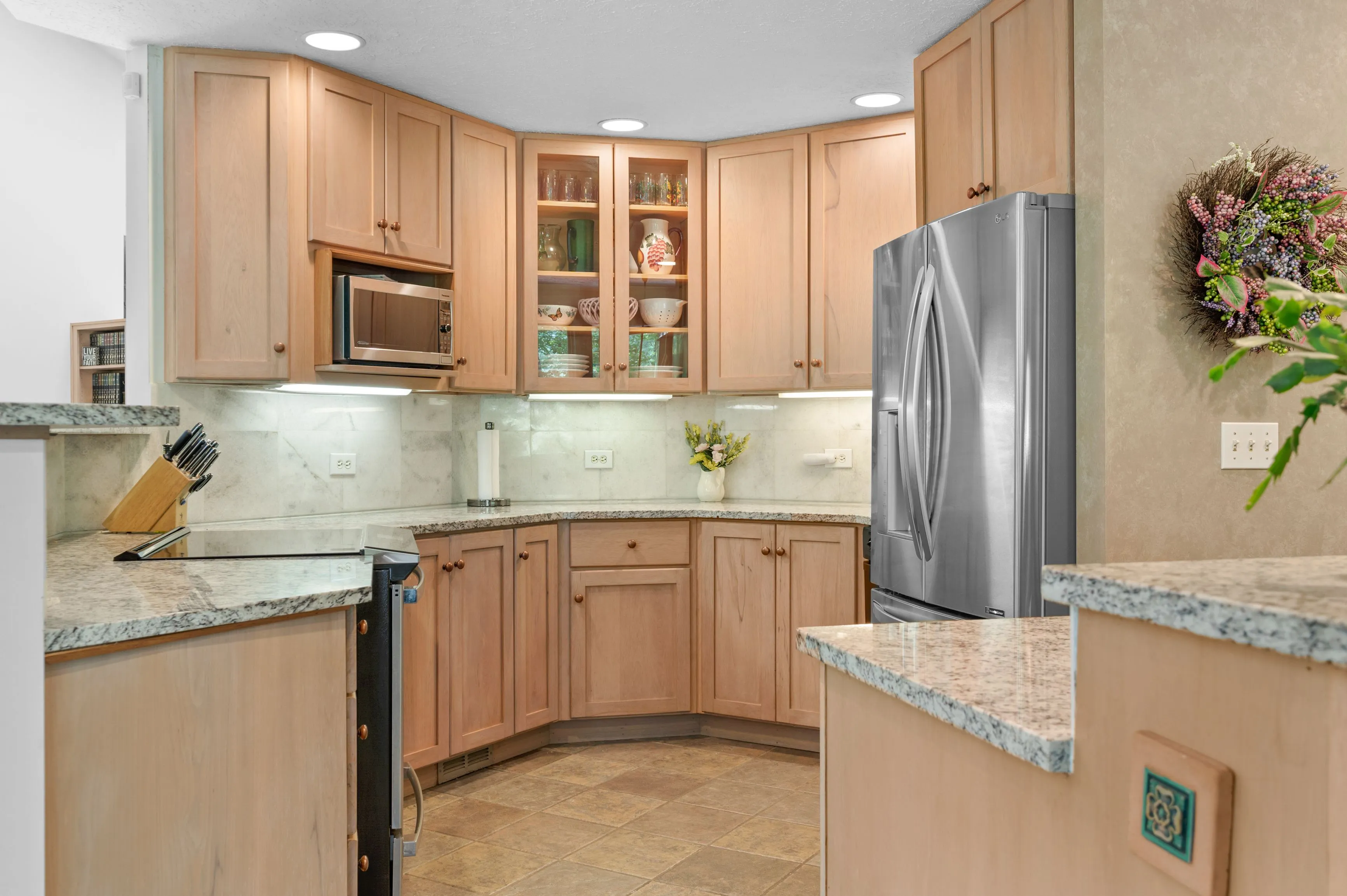 Modern kitchen interior with wooden cabinets, stainless steel refrigerator, and granite countertops.
