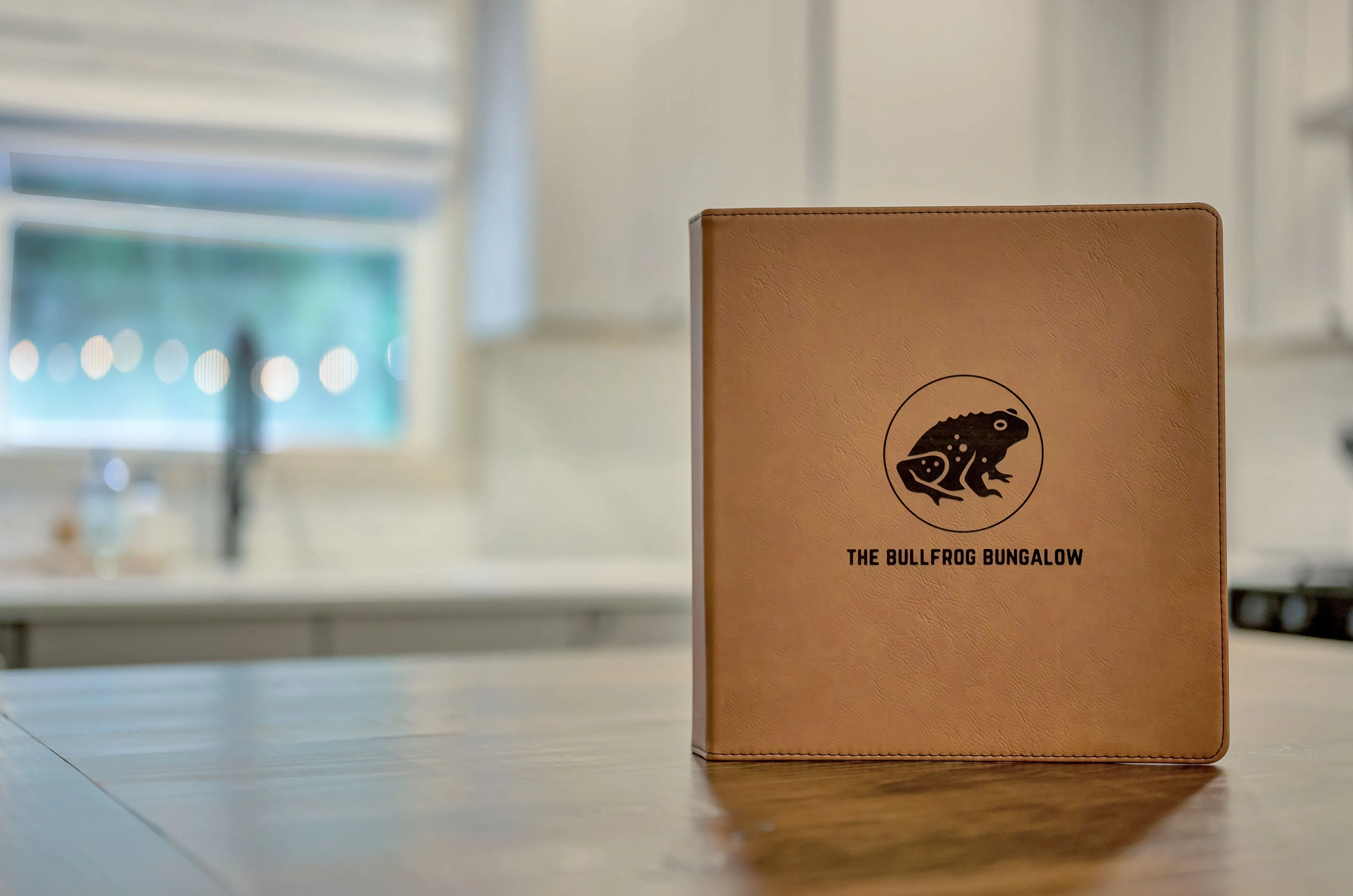 Leather-bound menu cover with a bullfrog logo for 'The Bullfrog Bungalow' on a wooden countertop in a kitchen setting.