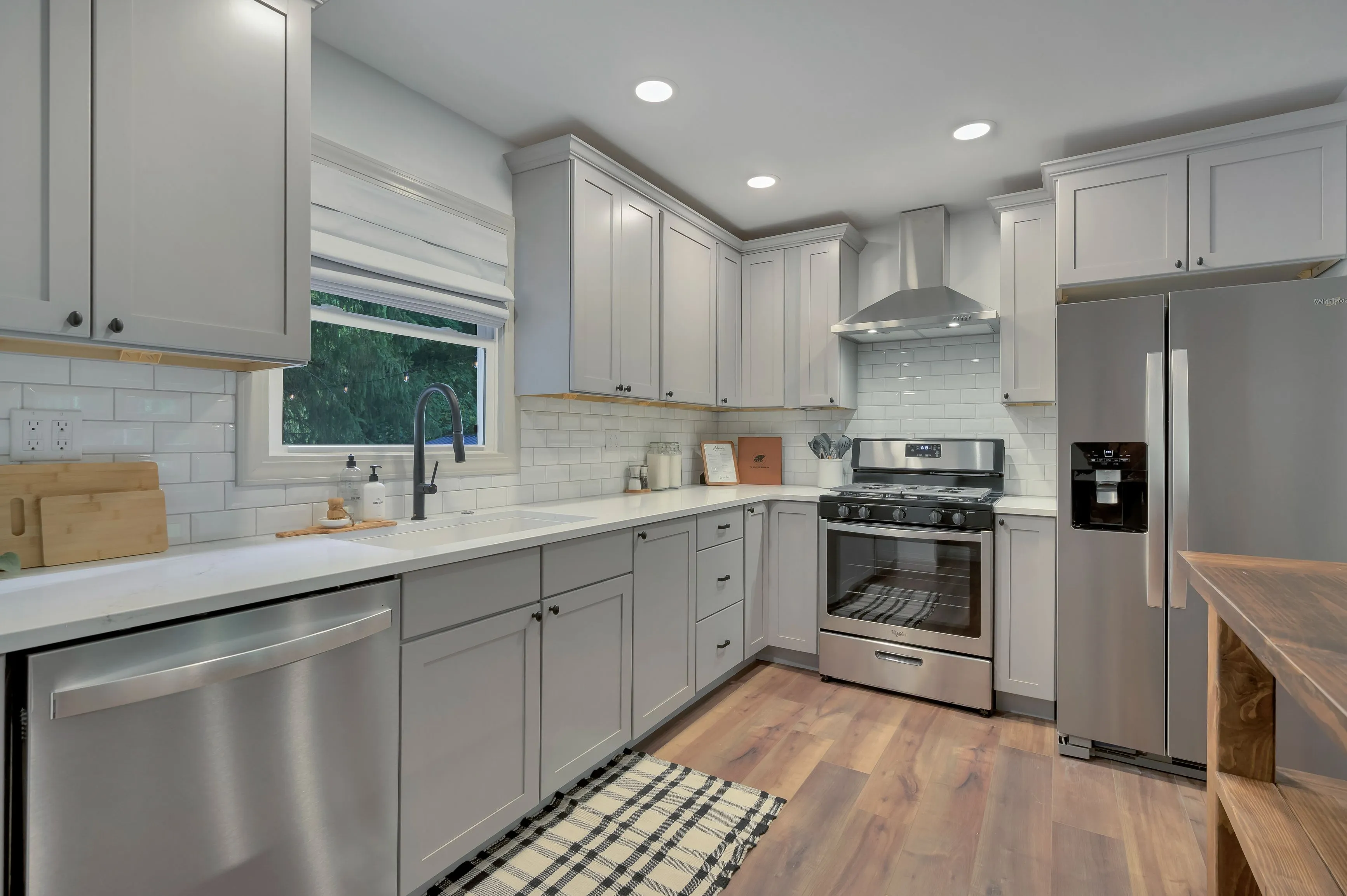 Modern kitchen interior with white cabinetry, stainless steel appliances, subway tile backsplash, and wood flooring.