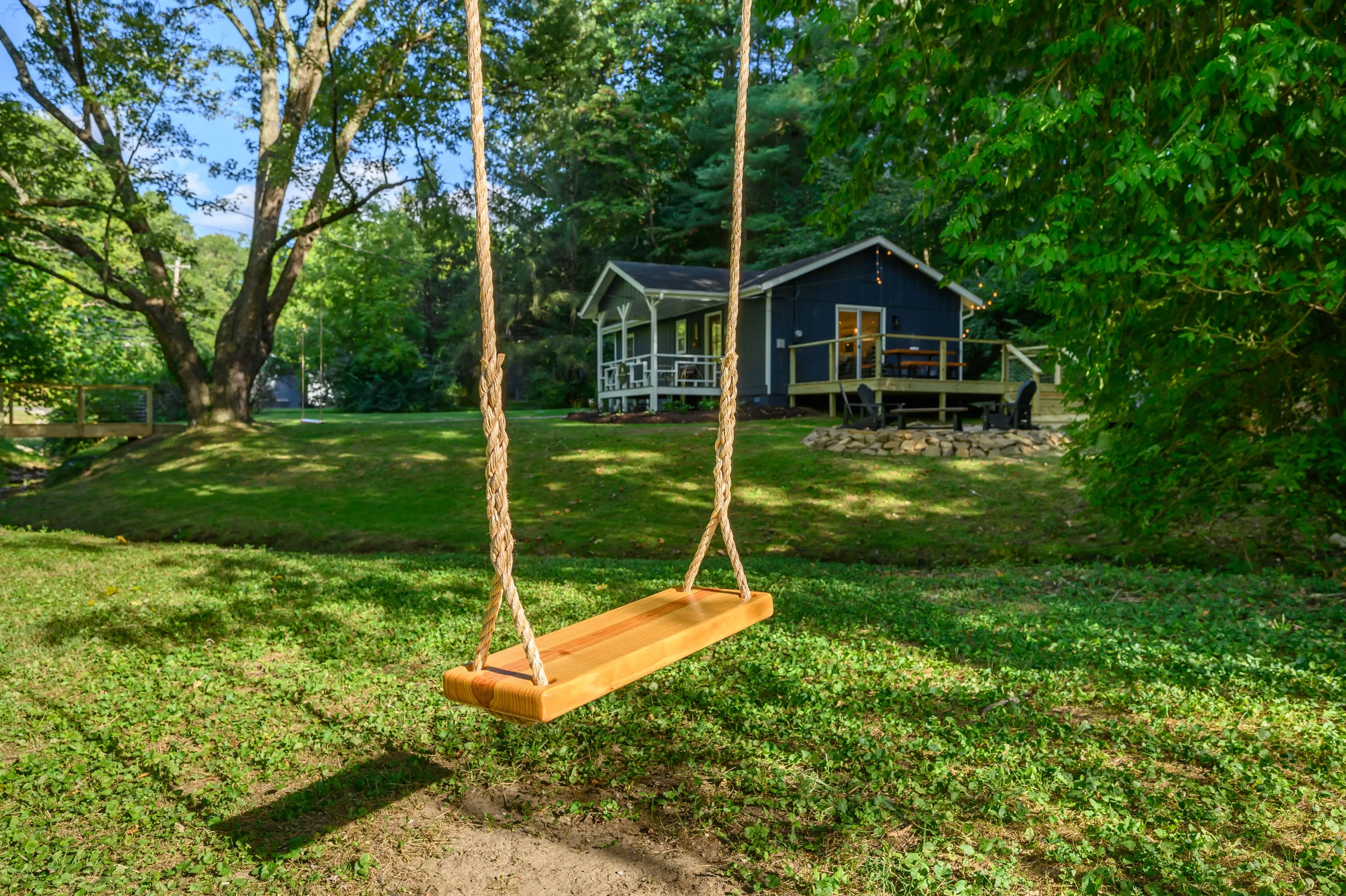 Wooden swing hanging from a tree in a lush backyard with a cozy house in the background.