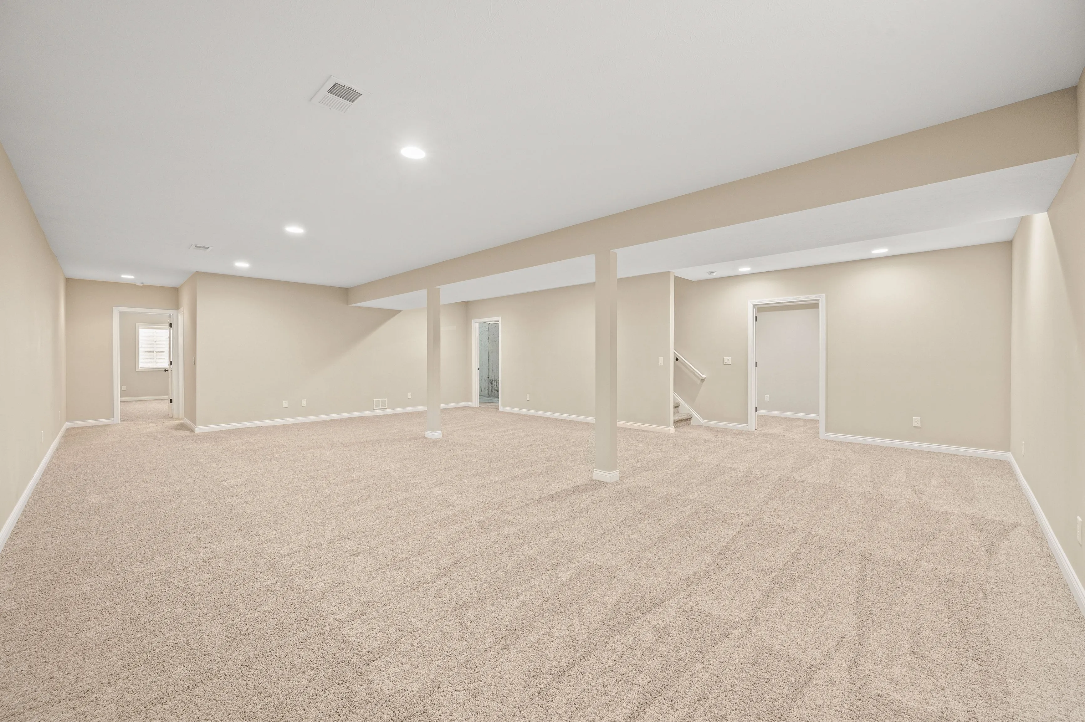Spacious empty basement room with carpeted floors and recessed lighting.