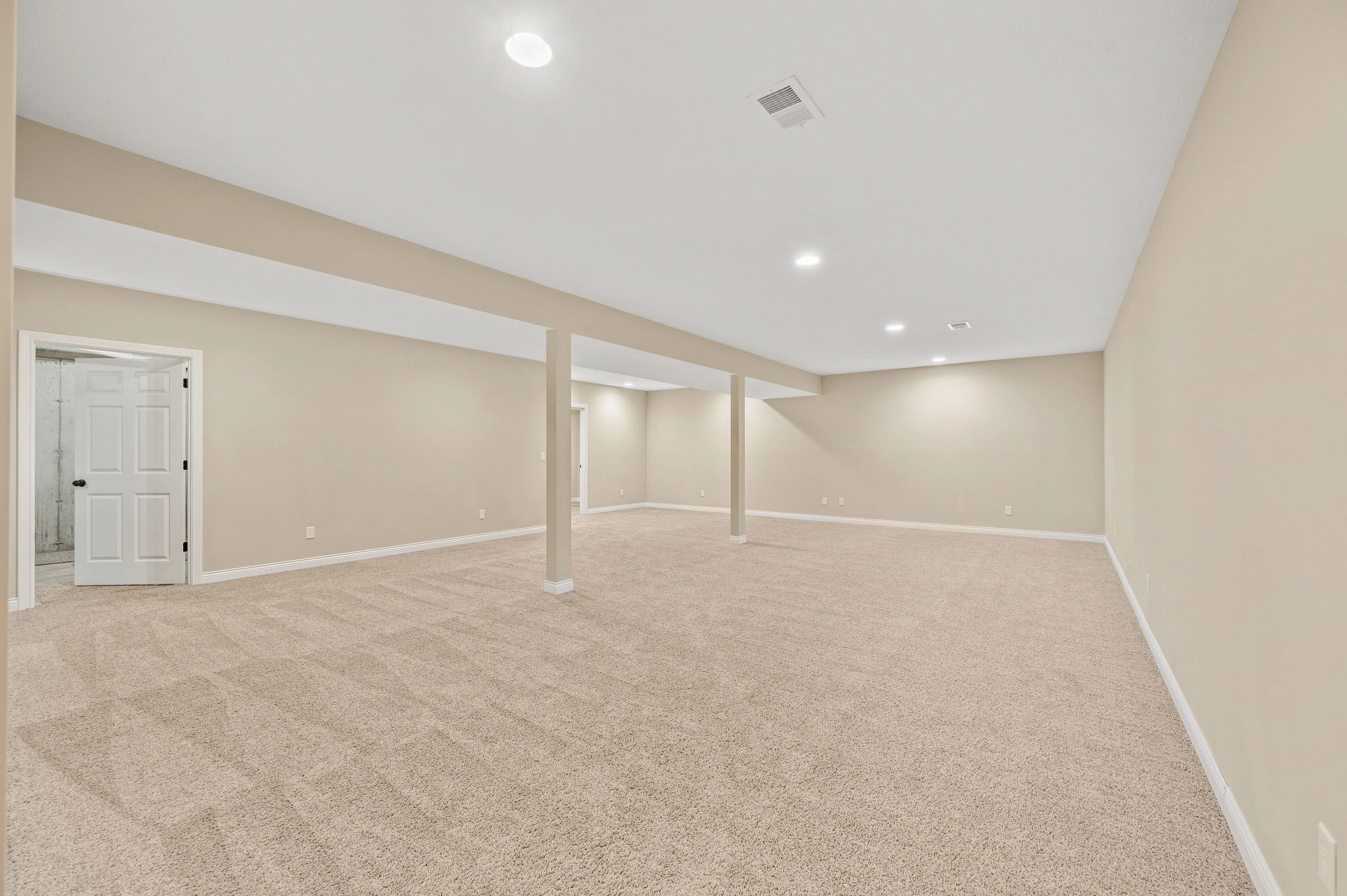Interior of an empty basement room with beige carpet, white walls, and multiple support columns.