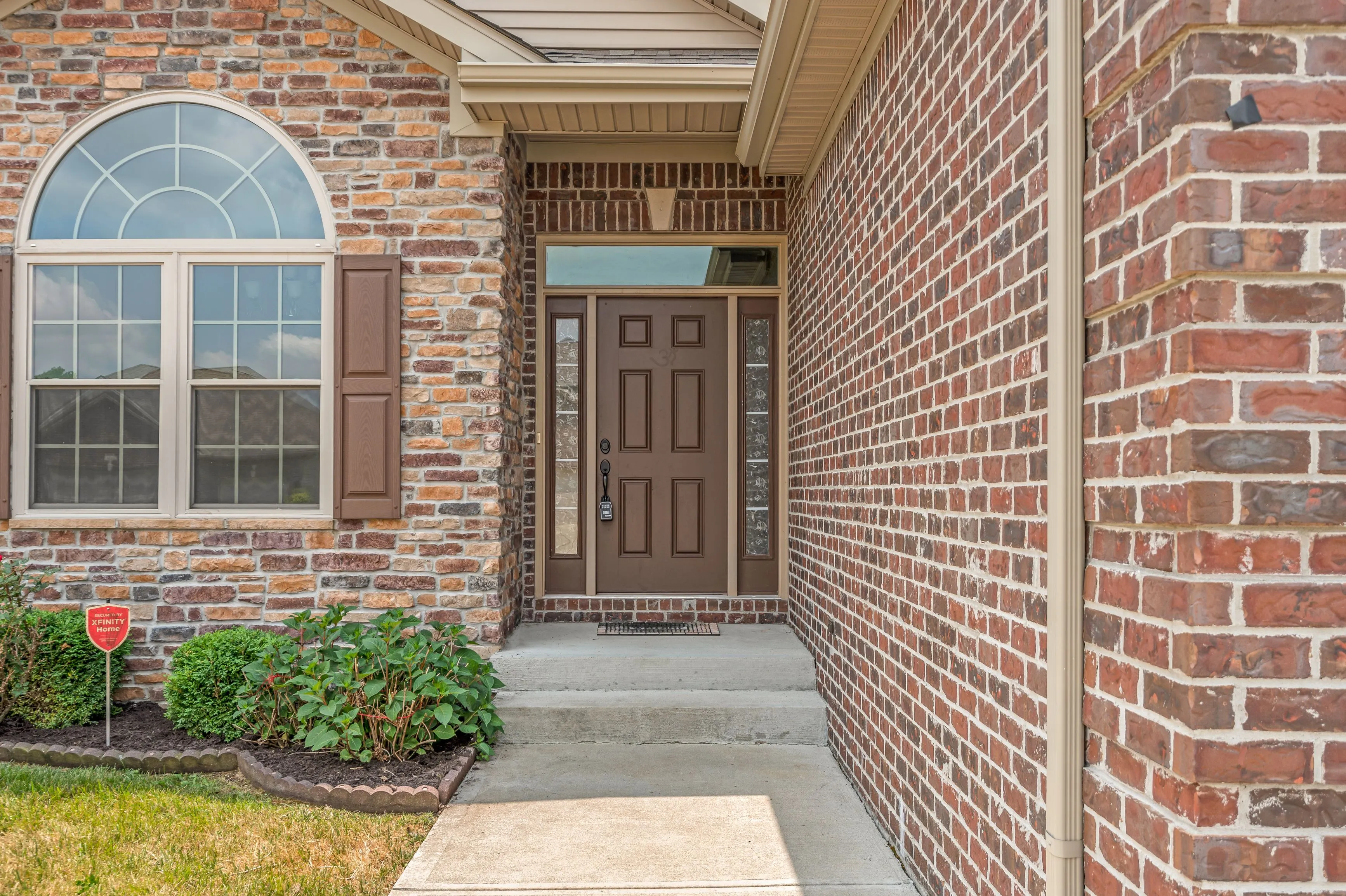 Exterior view of a residential home entrance with a brown door, brick walls, and a pathway leading up to the porch.
