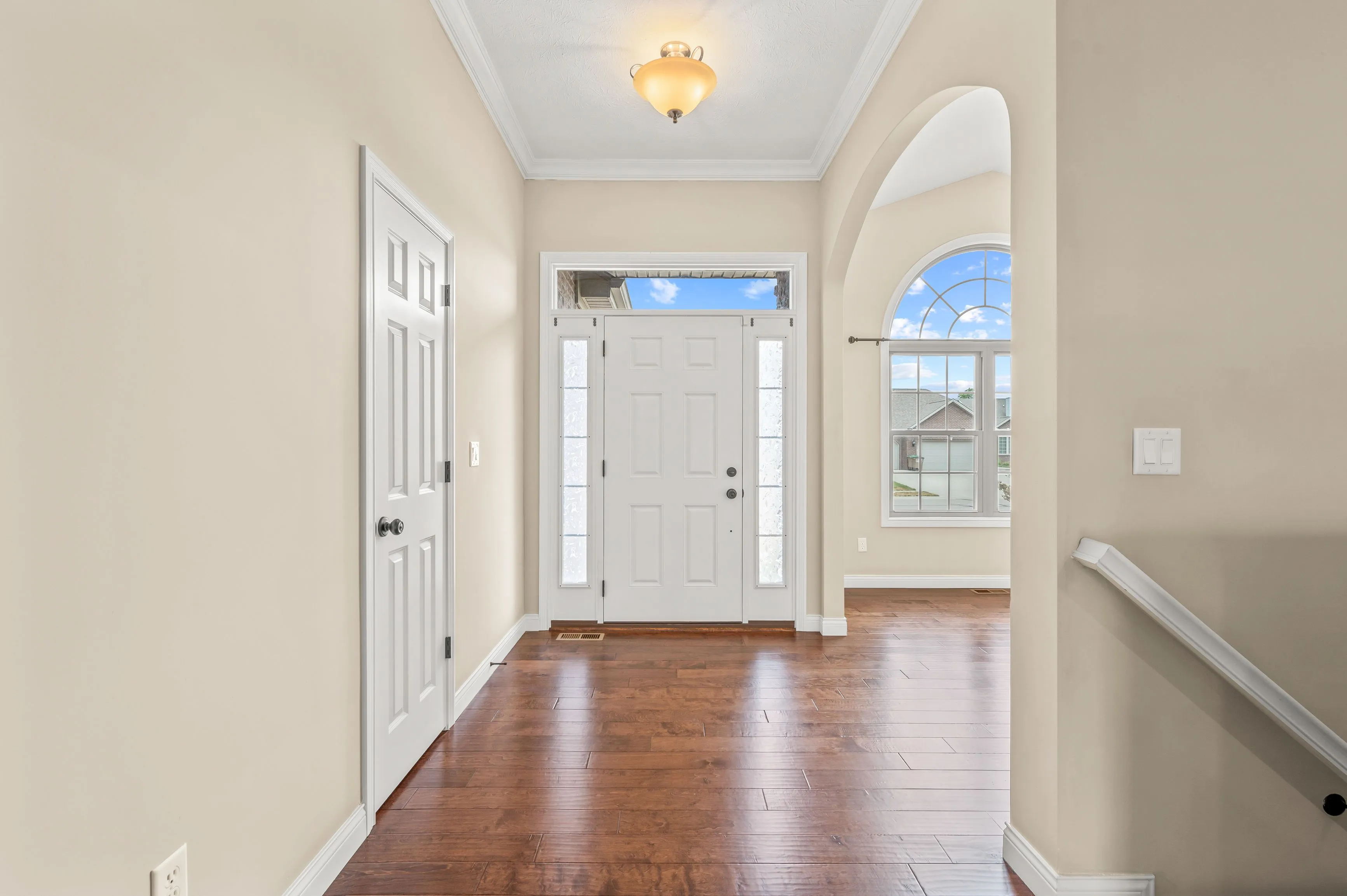 Bright entry hallway in a home with wooden floors, white walls, and a front door with sidelights.