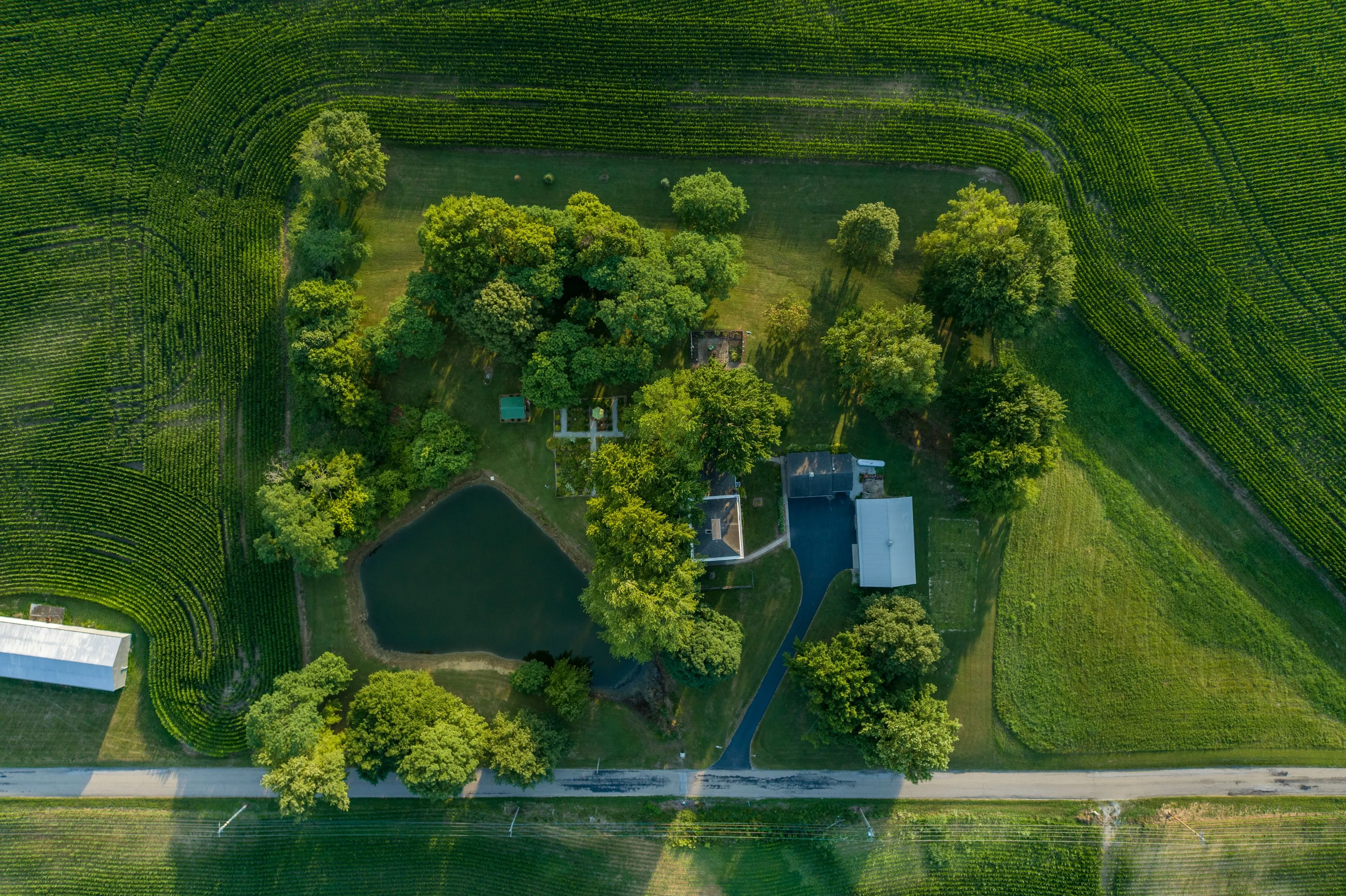 Aerial view of a lush green property with a pond surrounded by farmland and a road.