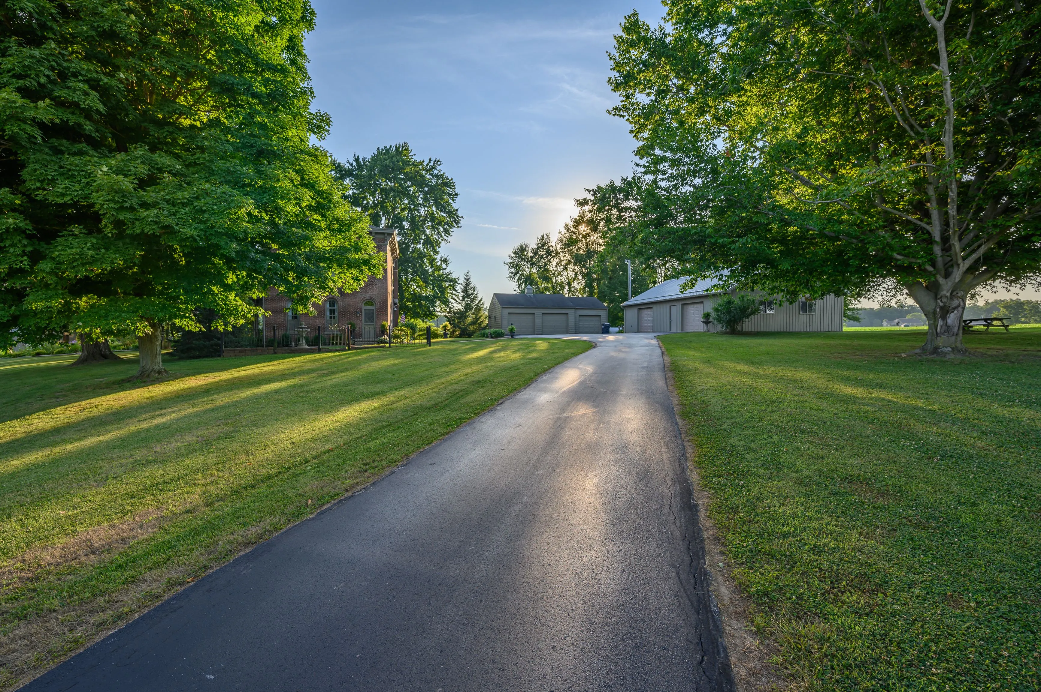 A tree-lined driveway leading to buildings with a setting sun casting a glow on the landscape.