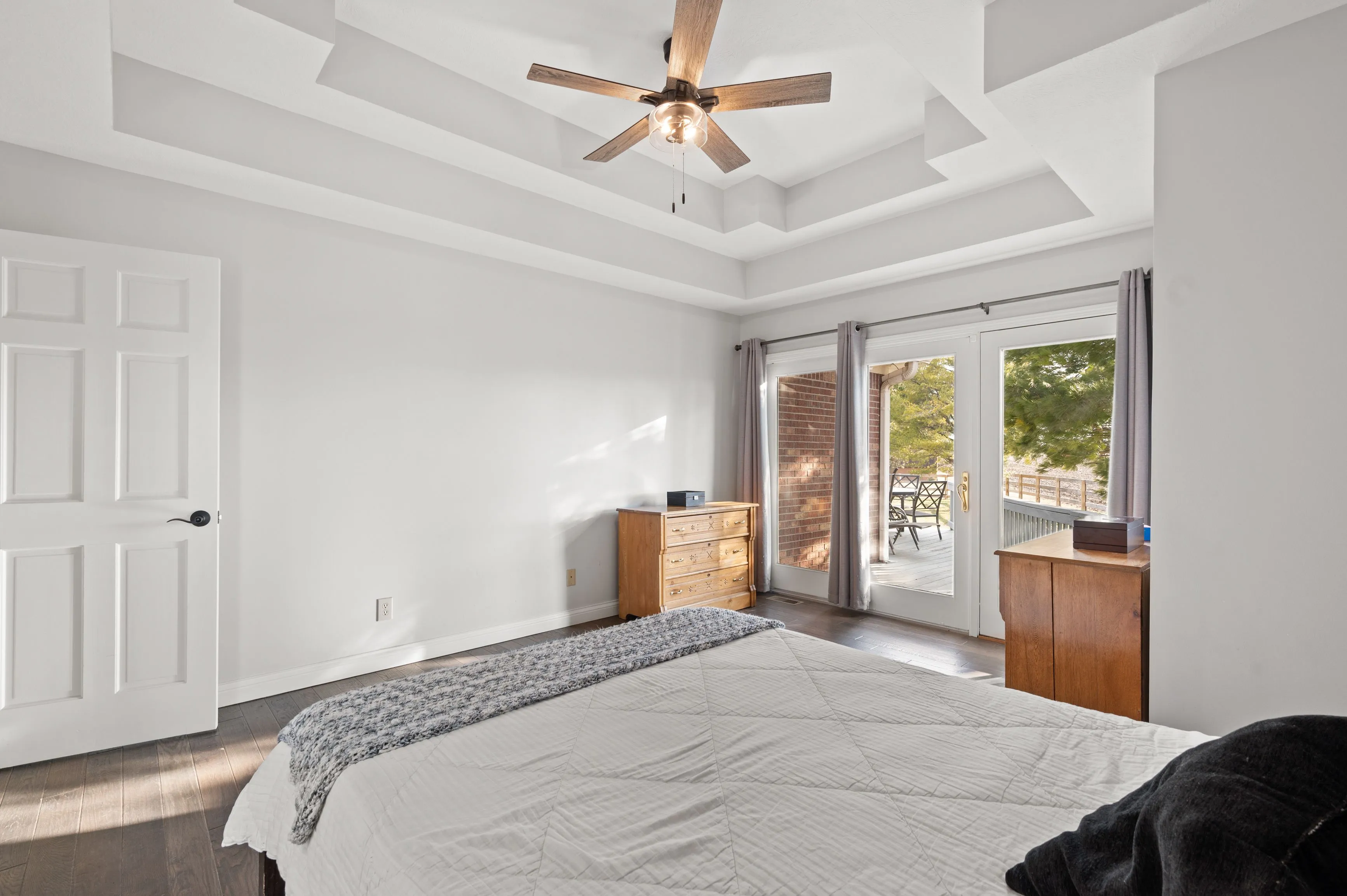 Bright bedroom with a vaulted ceiling and fan, hardwood floors, a sliding door leading to a balcony, and a simple dresser and bed with linens.