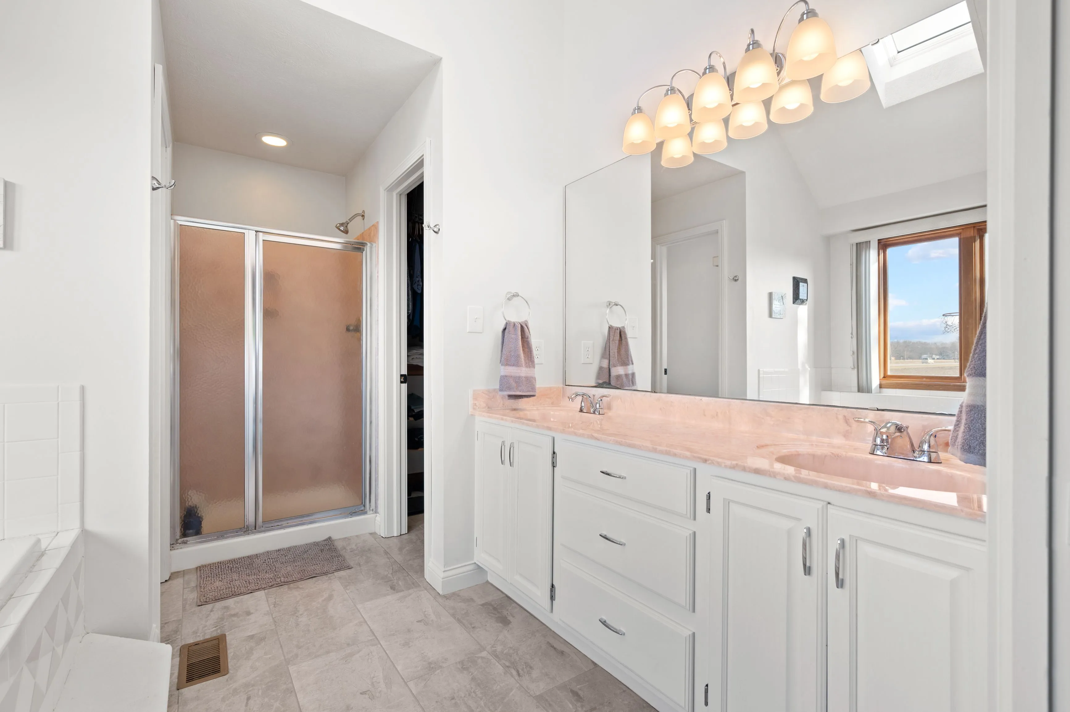 Bright modern bathroom with a double vanity, large mirror, frosted glass shower, and tiled flooring.