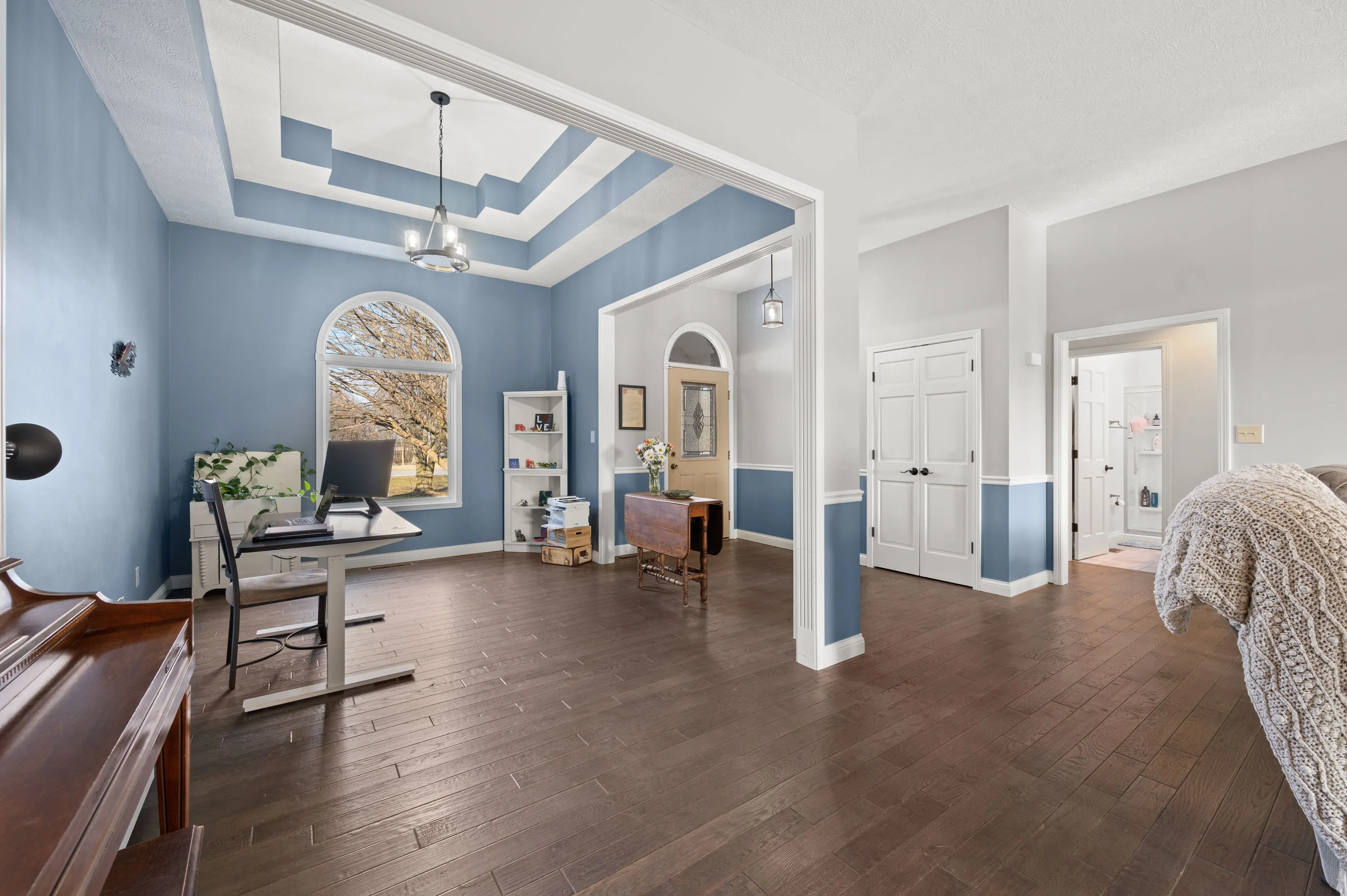 Bright and spacious room with blue walls, white trim, dark wooden flooring, and contemporary furniture including a standing desk and piano.