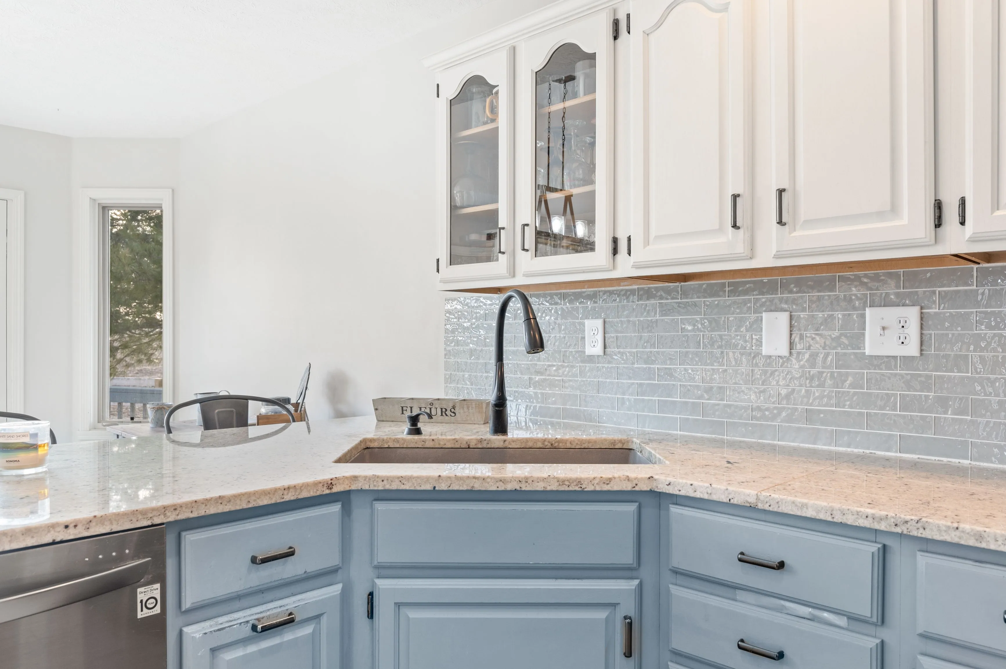 Modern kitchen interior with white upper cabinets and blue lower cabinets, granite countertops, and a subway tile backsplash.