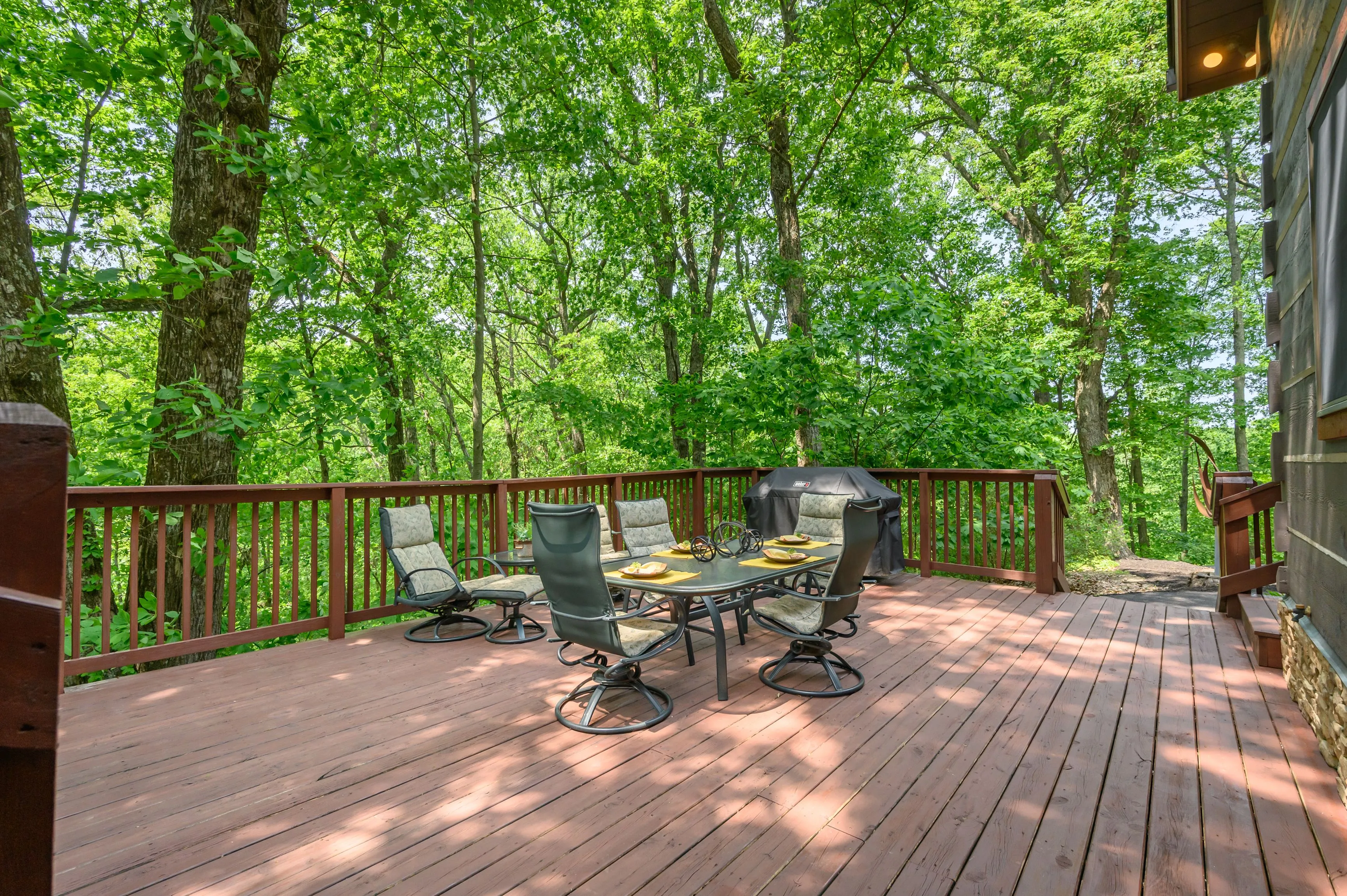 Wooden deck with outdoor furniture surrounded by lush green trees.