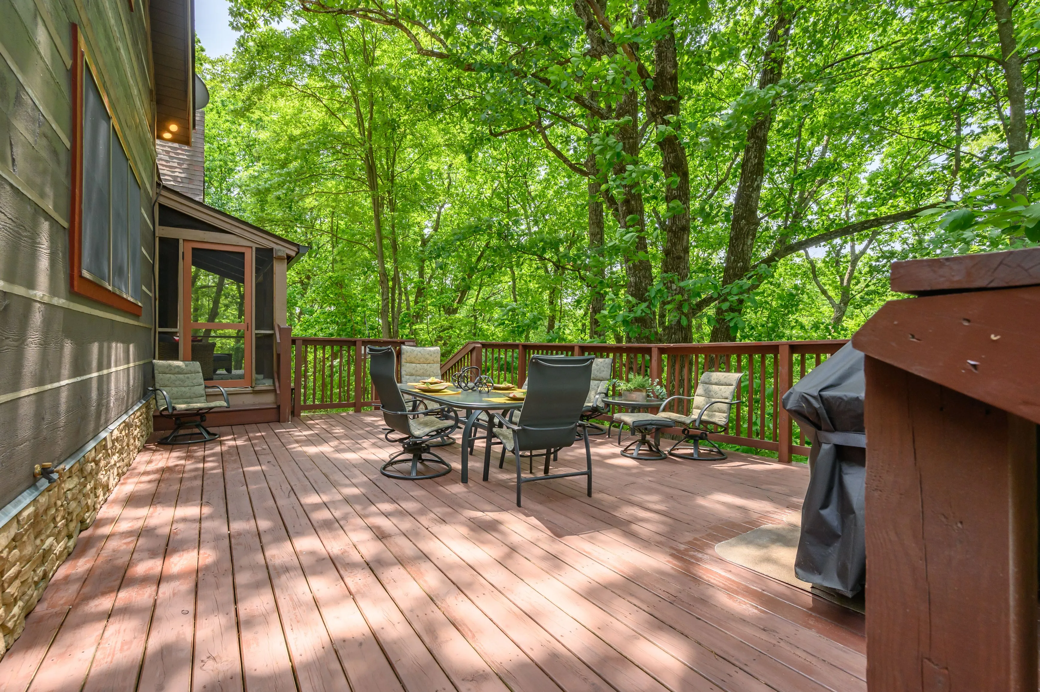 Spacious wooden deck with outdoor furniture surrounded by lush green trees.