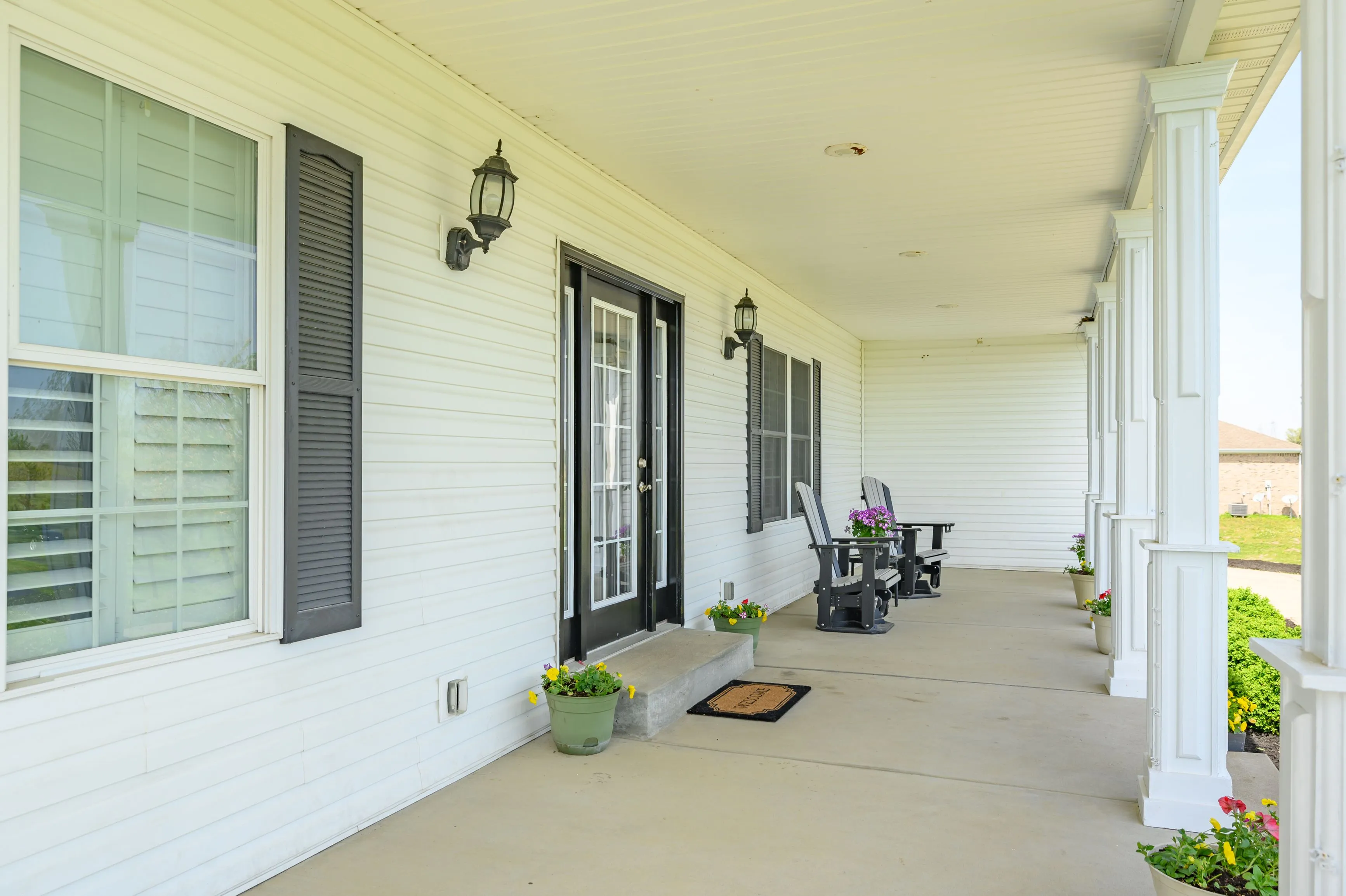 Bright and inviting covered residential porch with chairs, plants, and welcome mat.