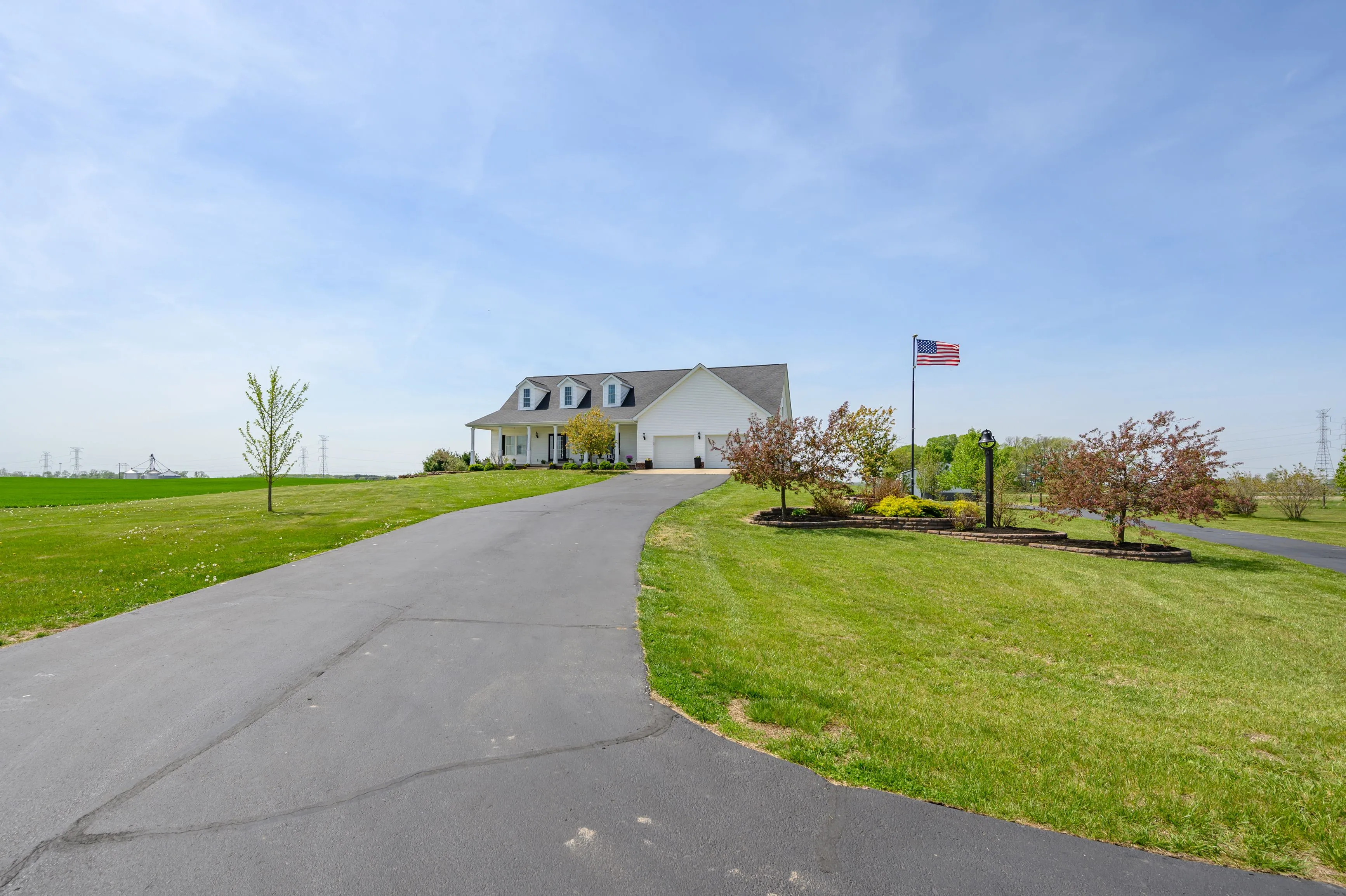 Curved driveway leading to a large house with an American flag under a clear blue sky.