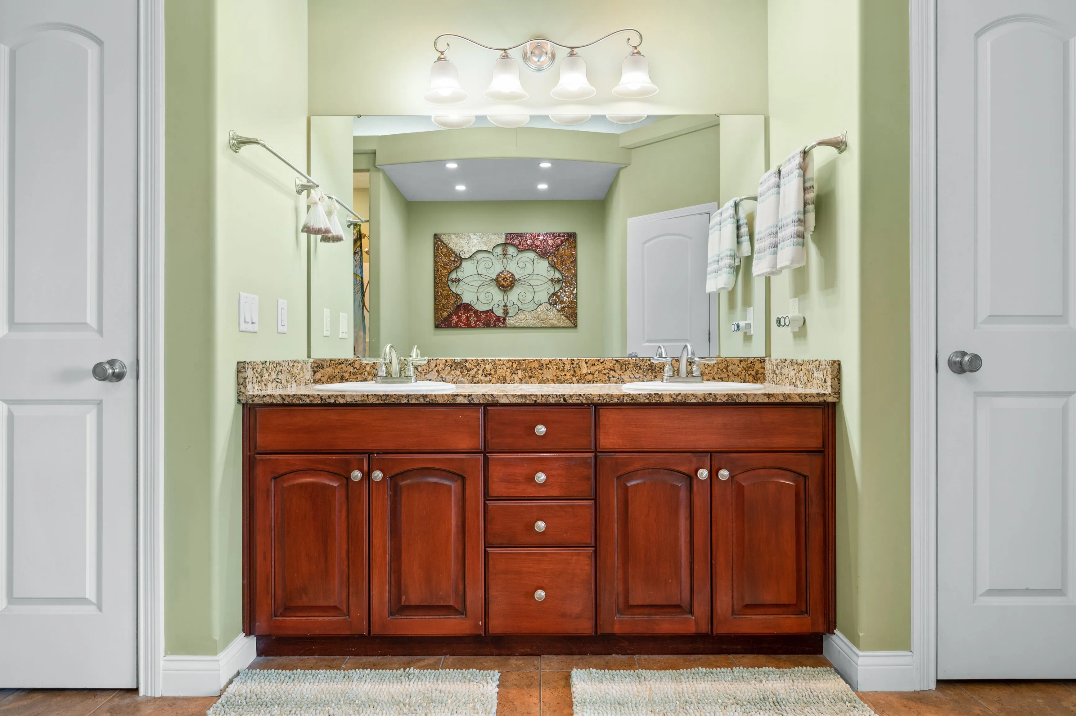 Elegant bathroom interior with cherry wood cabinets, granite countertop, and dual sinks with large mirror above.