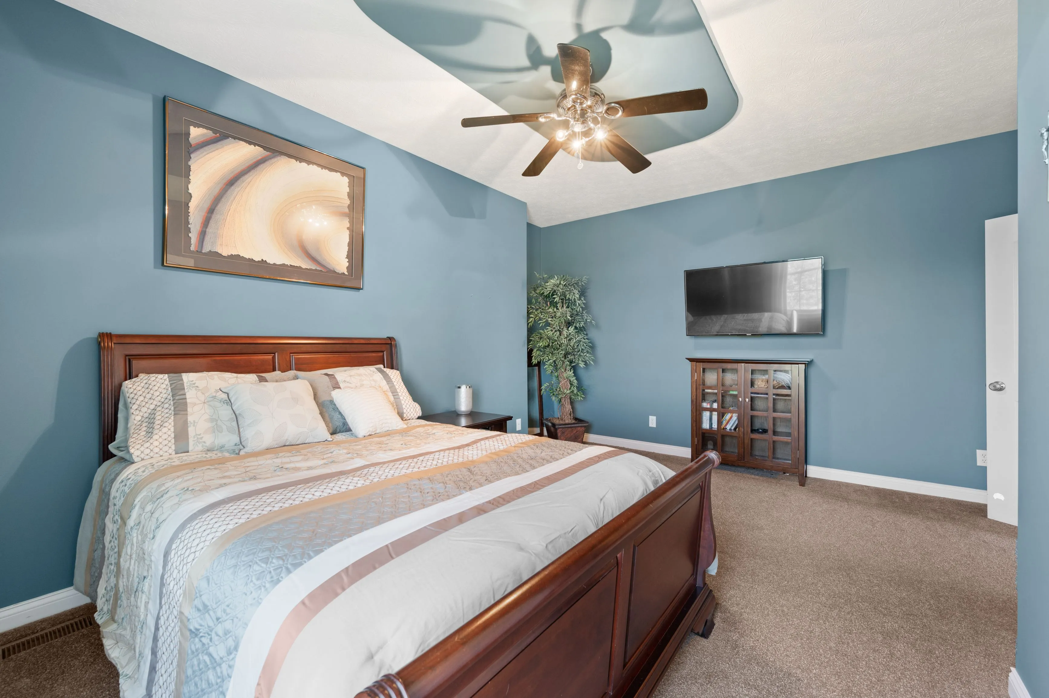 Elegantly furnished bedroom with a queen-sized bed, blue walls, ceiling fan, and a flat-screen TV.