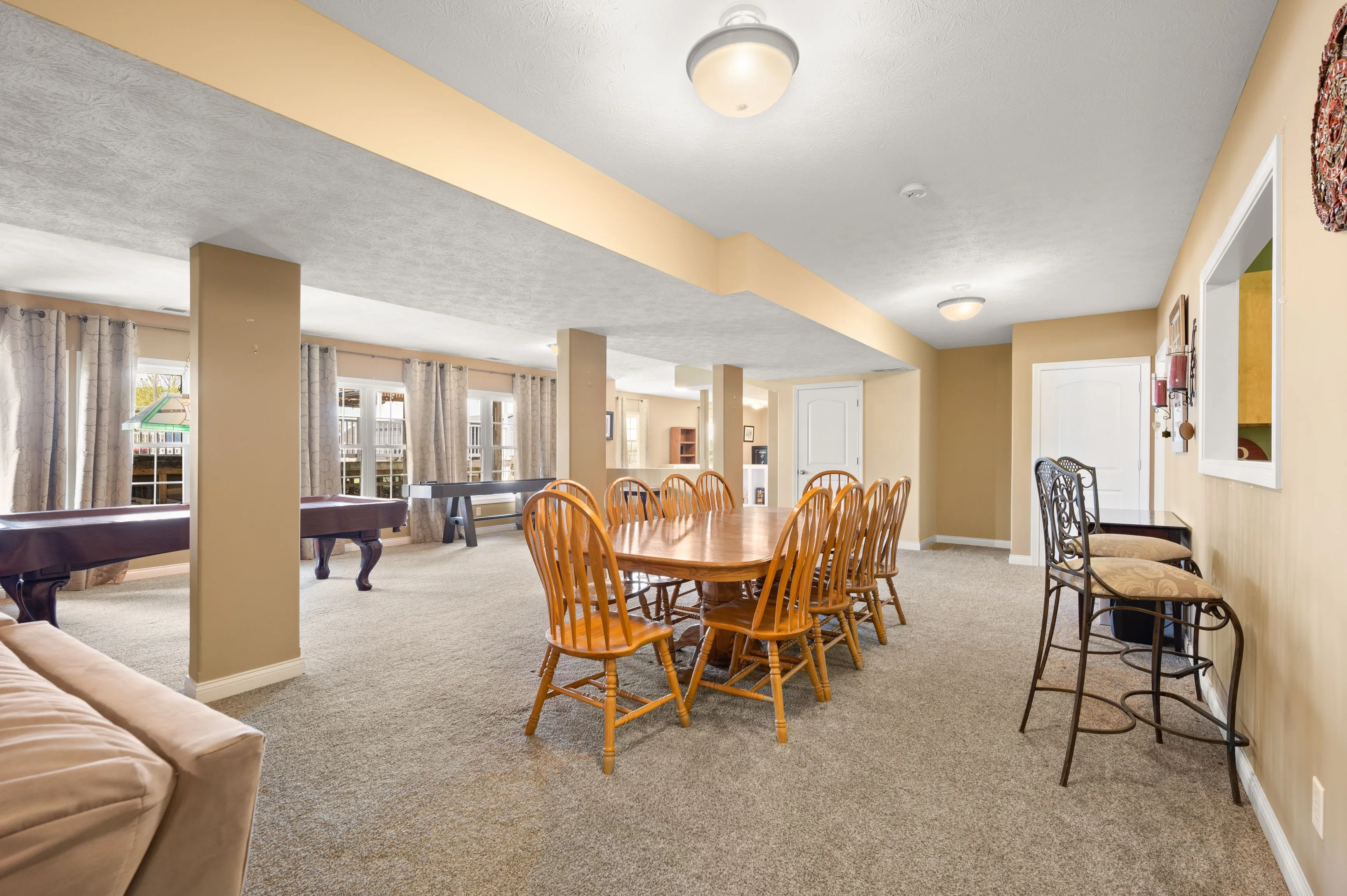 Spacious basement interior with dining area, pool table, and comfortable seating under warm lighting.
