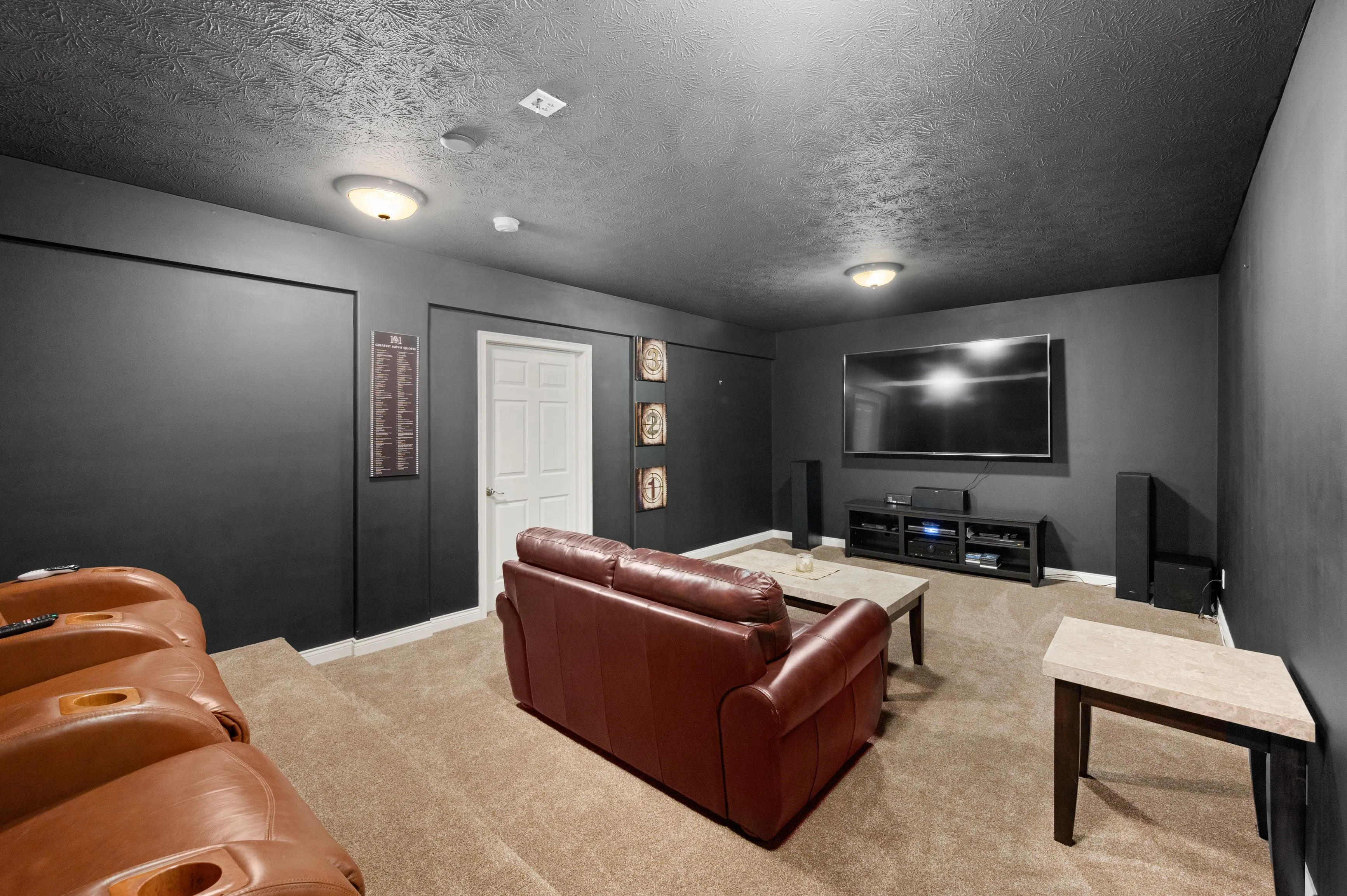 Modern home theater room with black walls, tiered brown leather seating, large flat-screen TV, and recessed ceiling lighting.