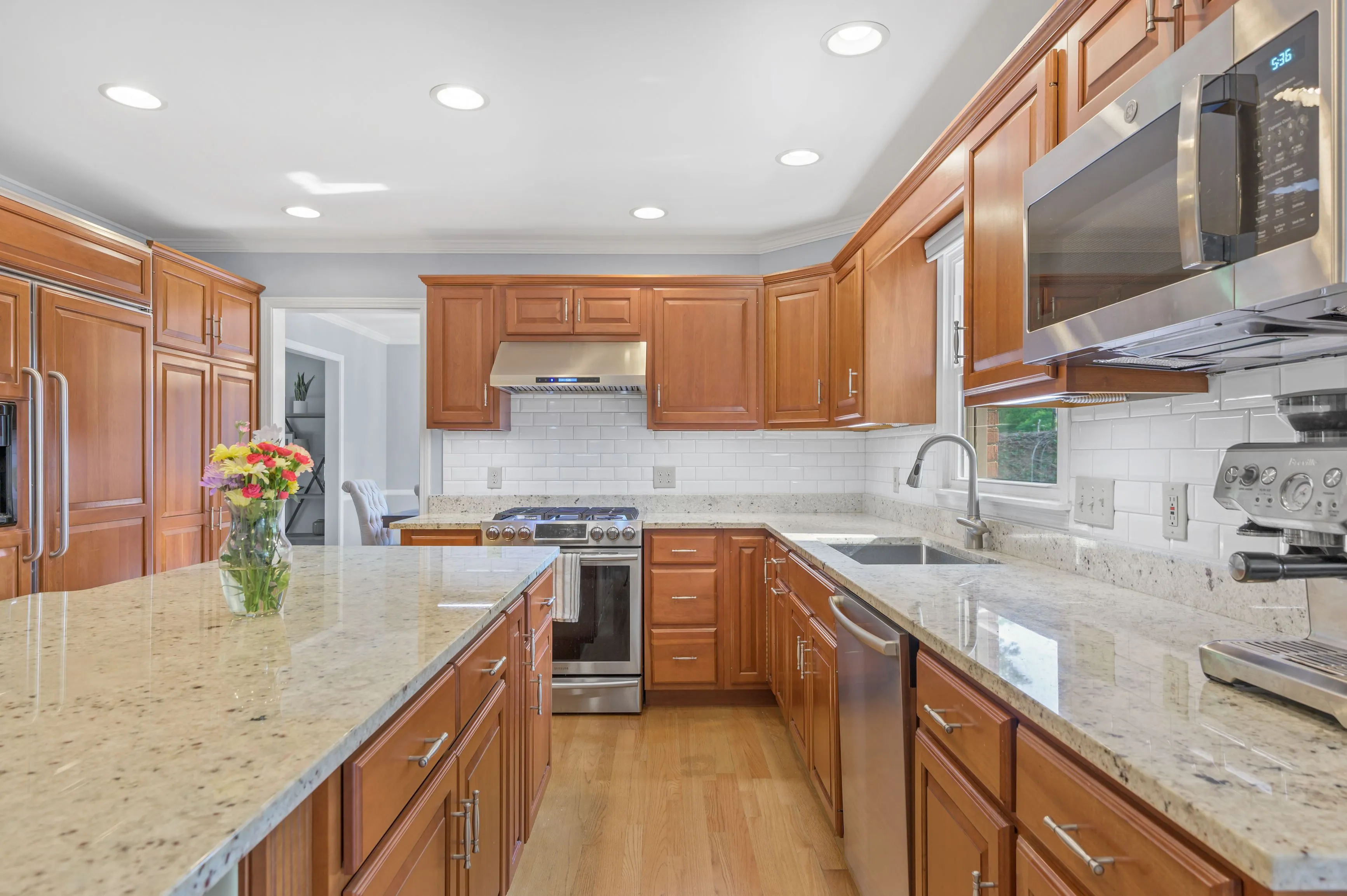 Spacious kitchen interior with wooden cabinets, granite countertops and modern stainless steel appliances.