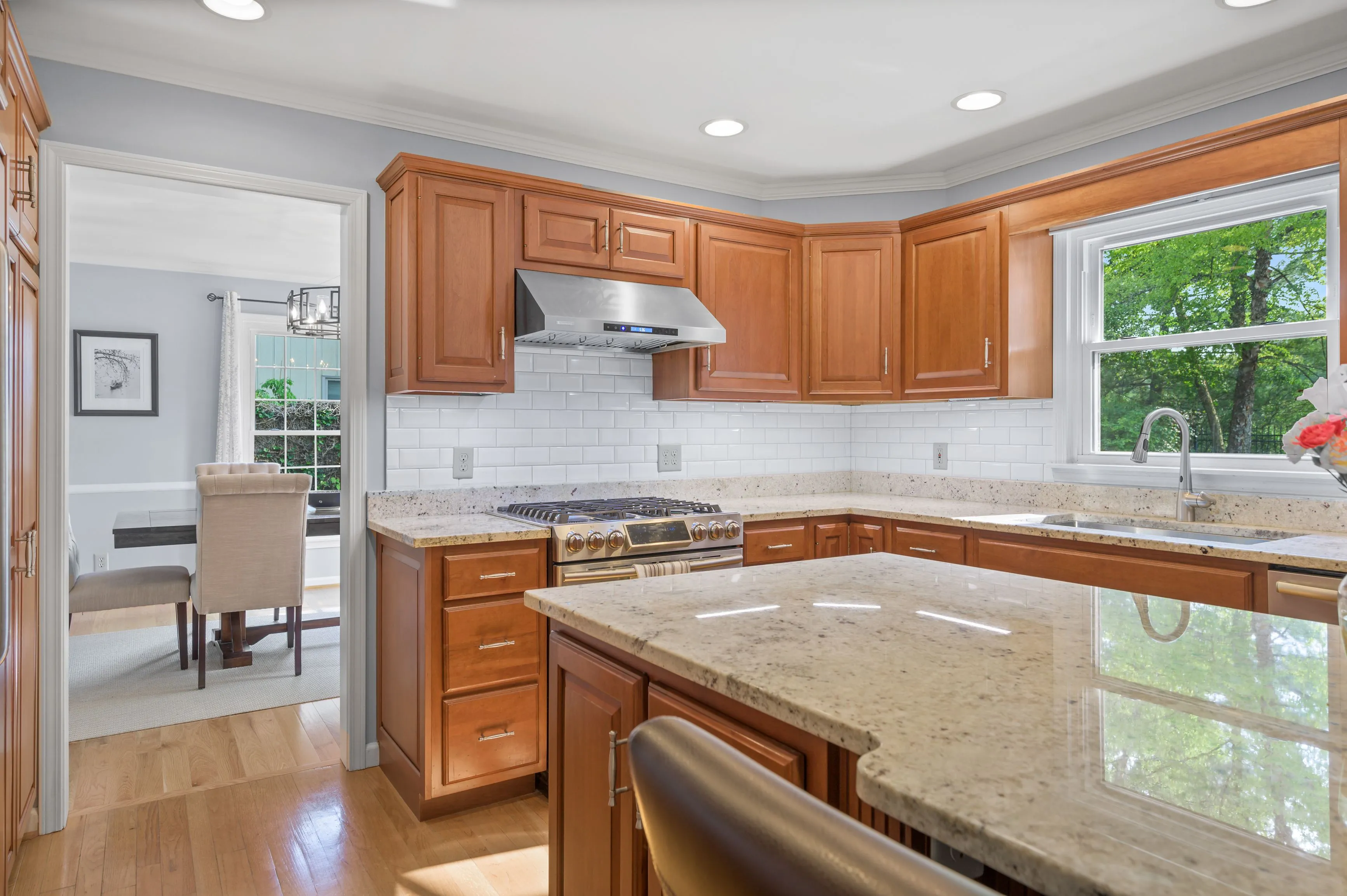 Spacious kitchen interior with wooden cabinets, granite countertops, and stainless steel appliances, featuring a central island and hardwood flooring.