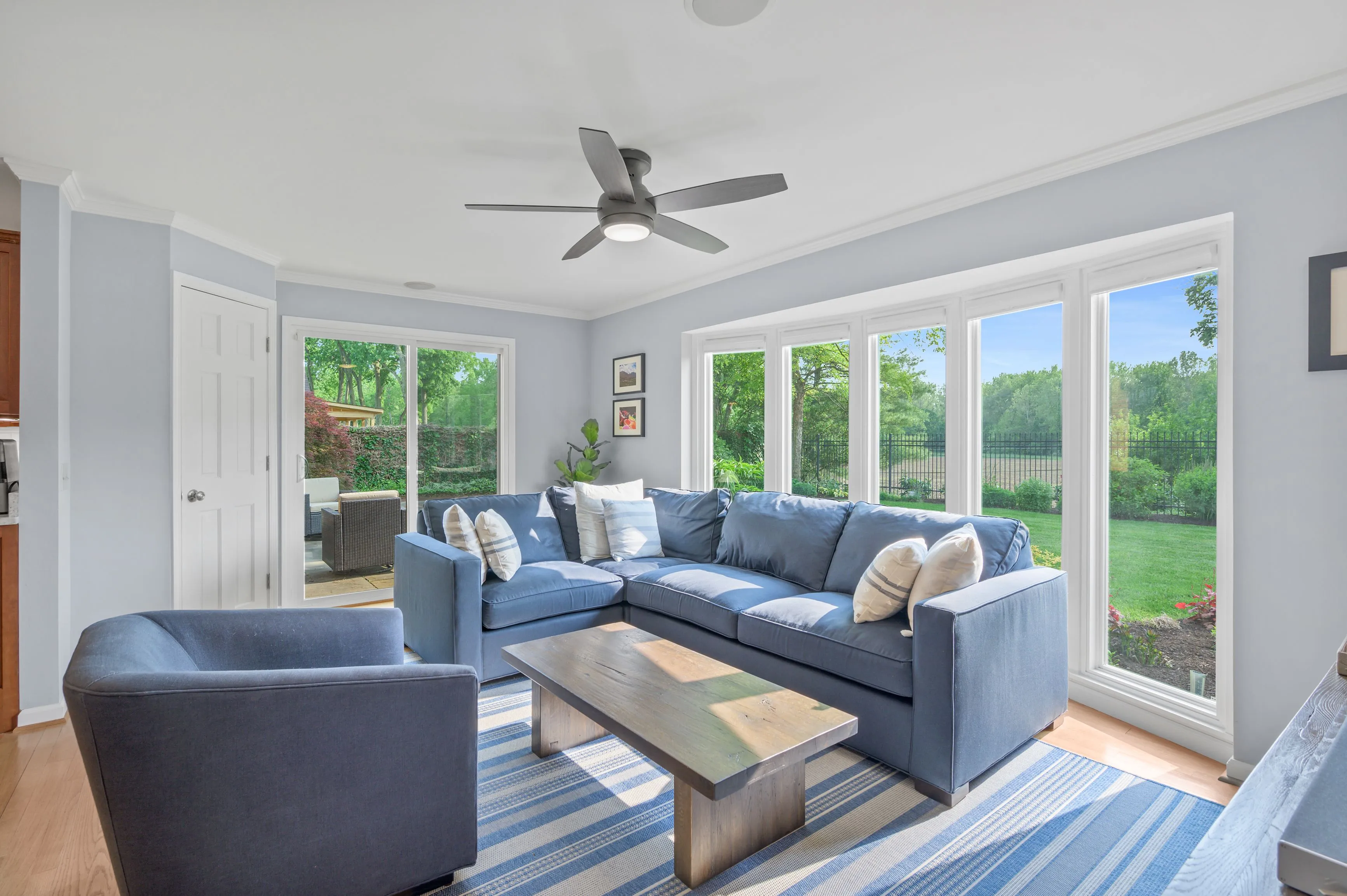 Bright living room with blue sofas, wooden coffee table, and large windows overlooking a green yard.