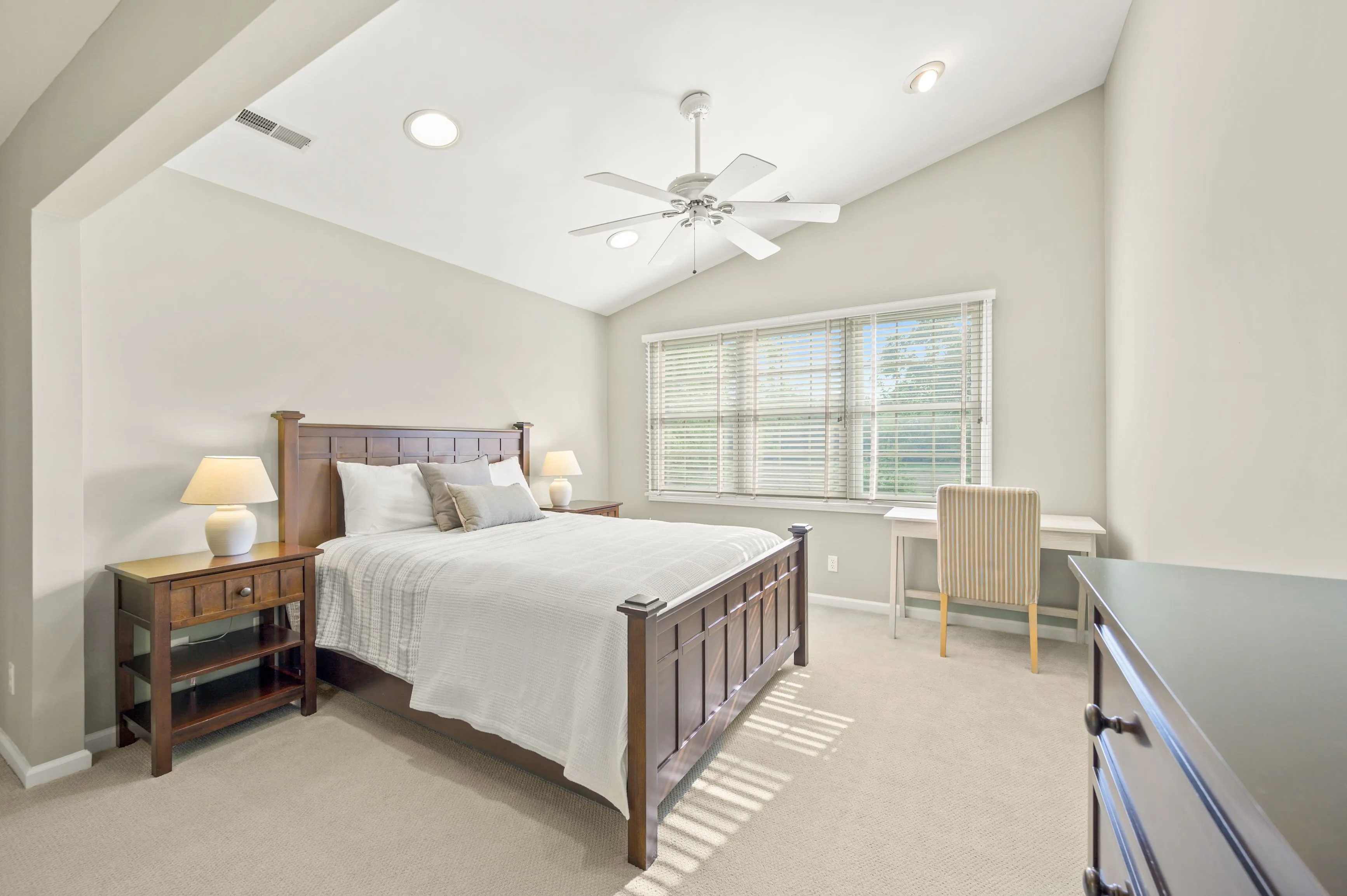Bright spacious bedroom with a king-sized bed, large windows, and a ceiling fan.