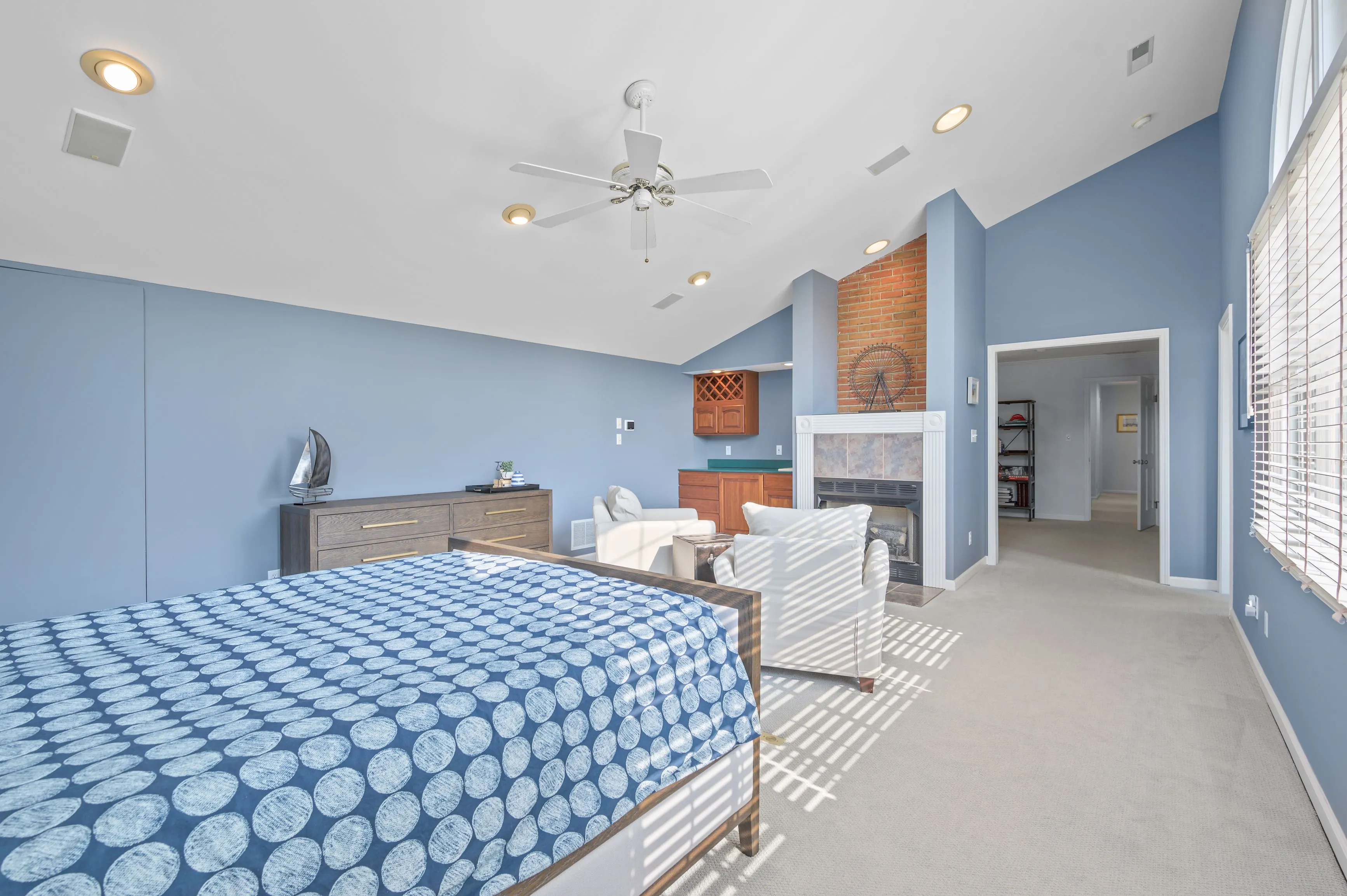 Spacious bedroom with blue walls, a patterned bedspread, ceiling fan, and an ensuite bathroom entrance.