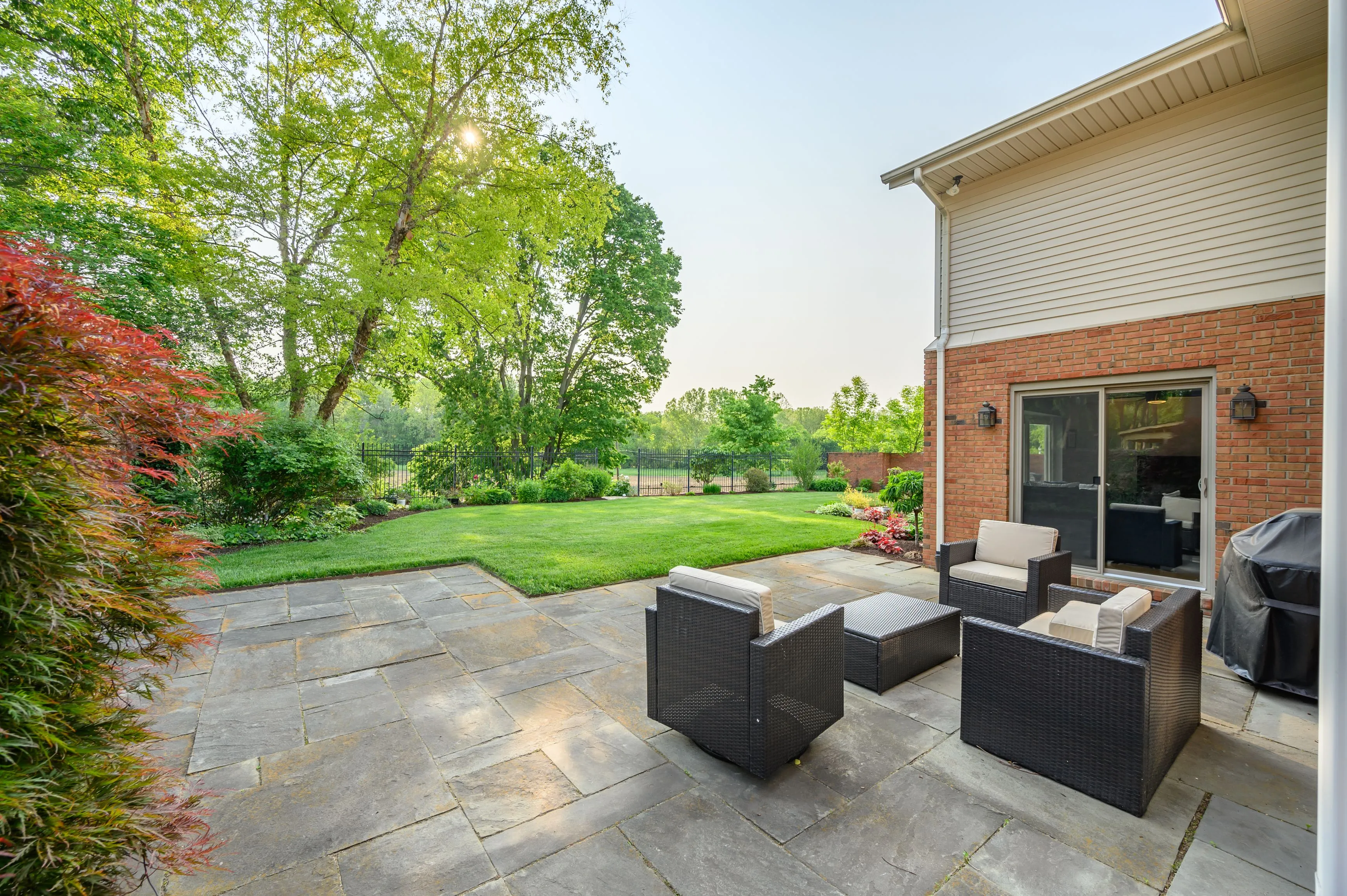 Patio furniture on stone pavers with a well-manicured lawn and trees in the background.