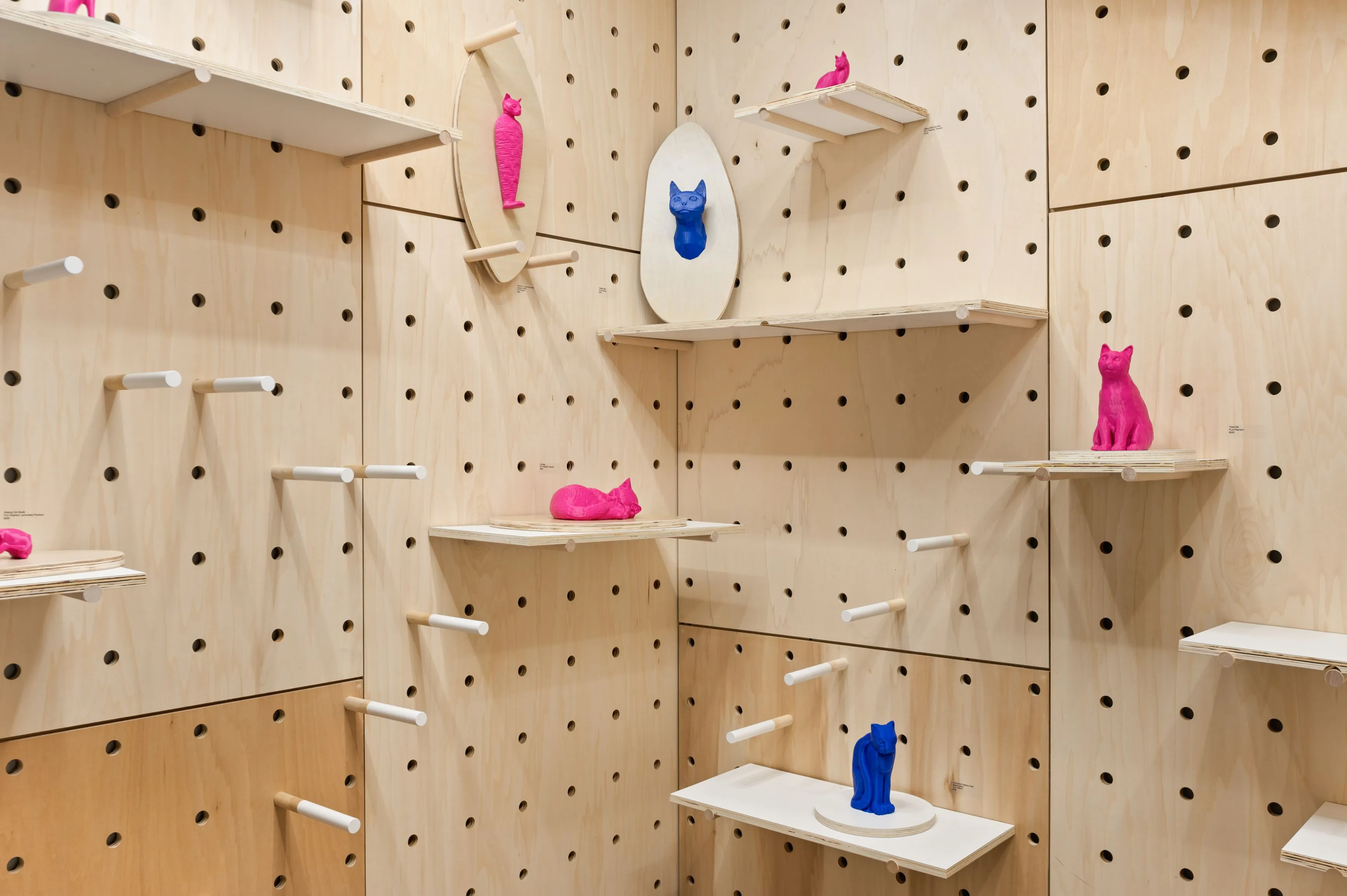 Interior of a room with pegboard walls and floating shelves holding various pink and blue abstract sculptures.