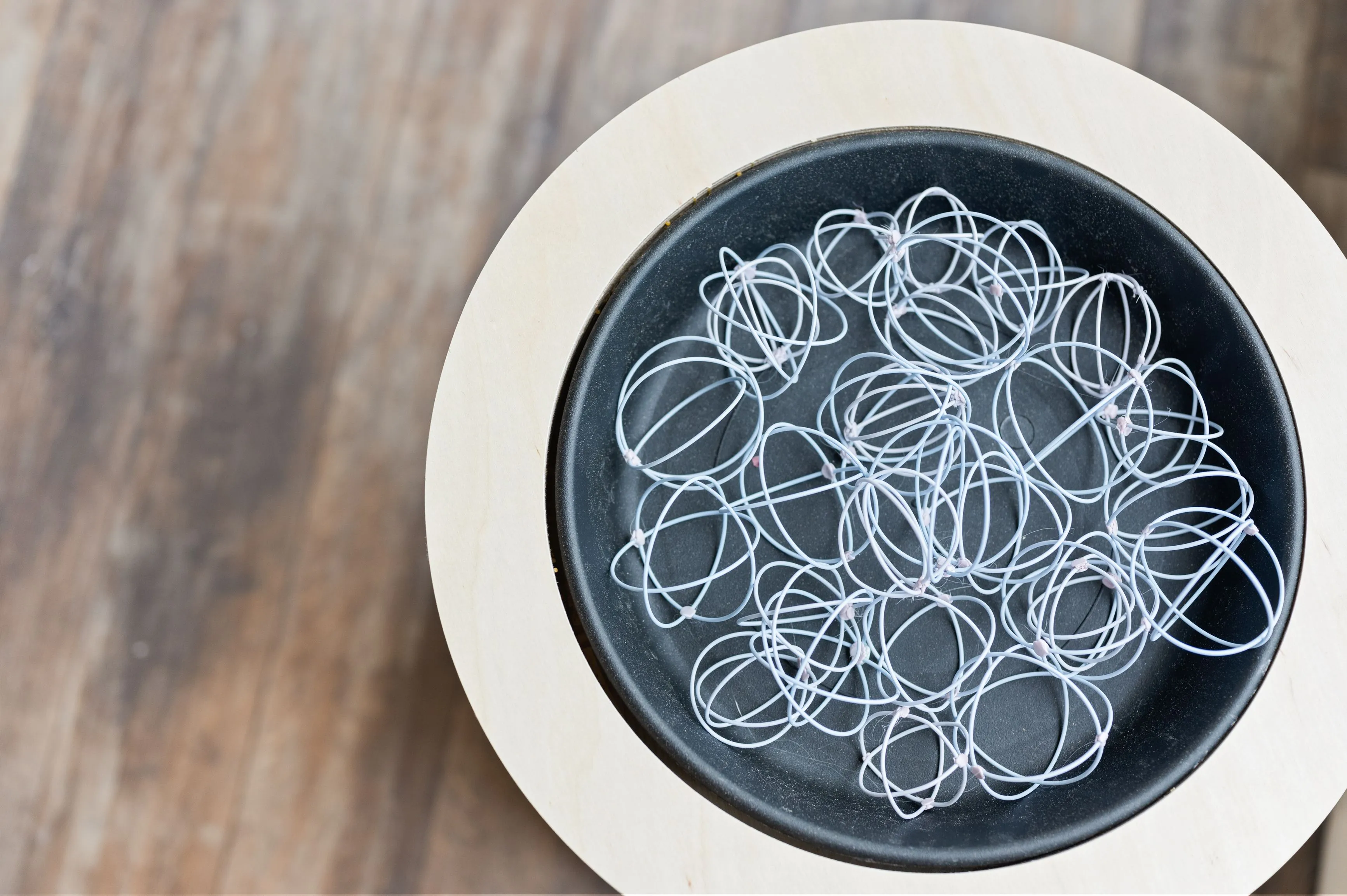 Bowl of assorted rubber bands on a wooden surface.