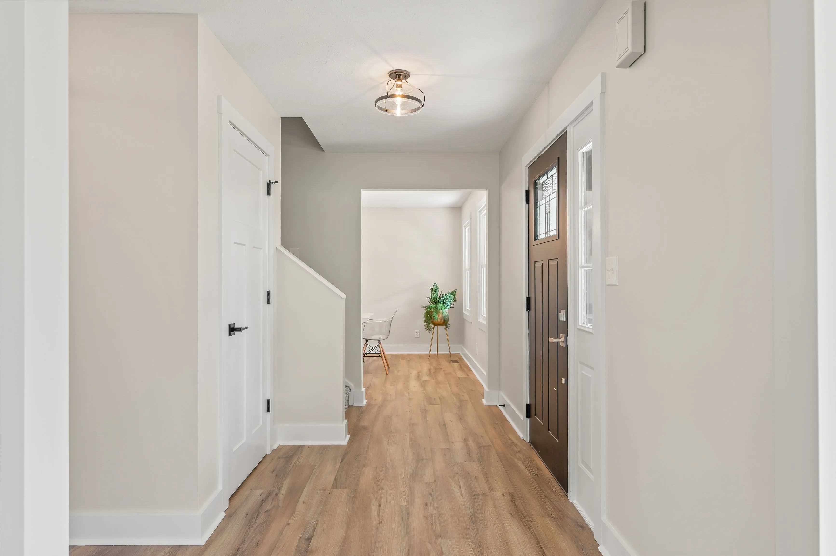 Bright and modern hallway interior with wooden flooring, white walls, and a front door with windows.