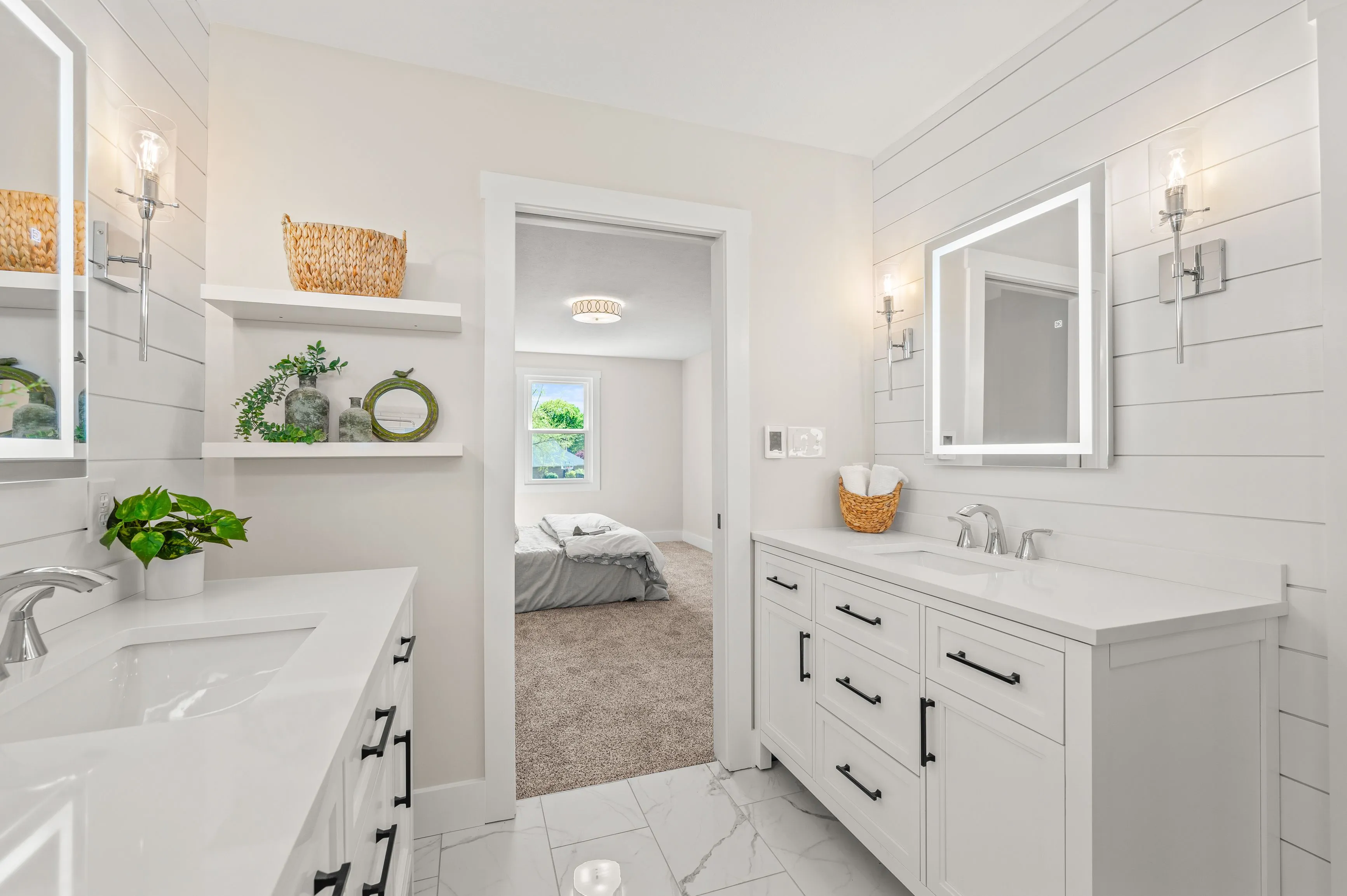 Modern bright bathroom interior with white cabinets, double sink, large mirror and a view into bedroom.