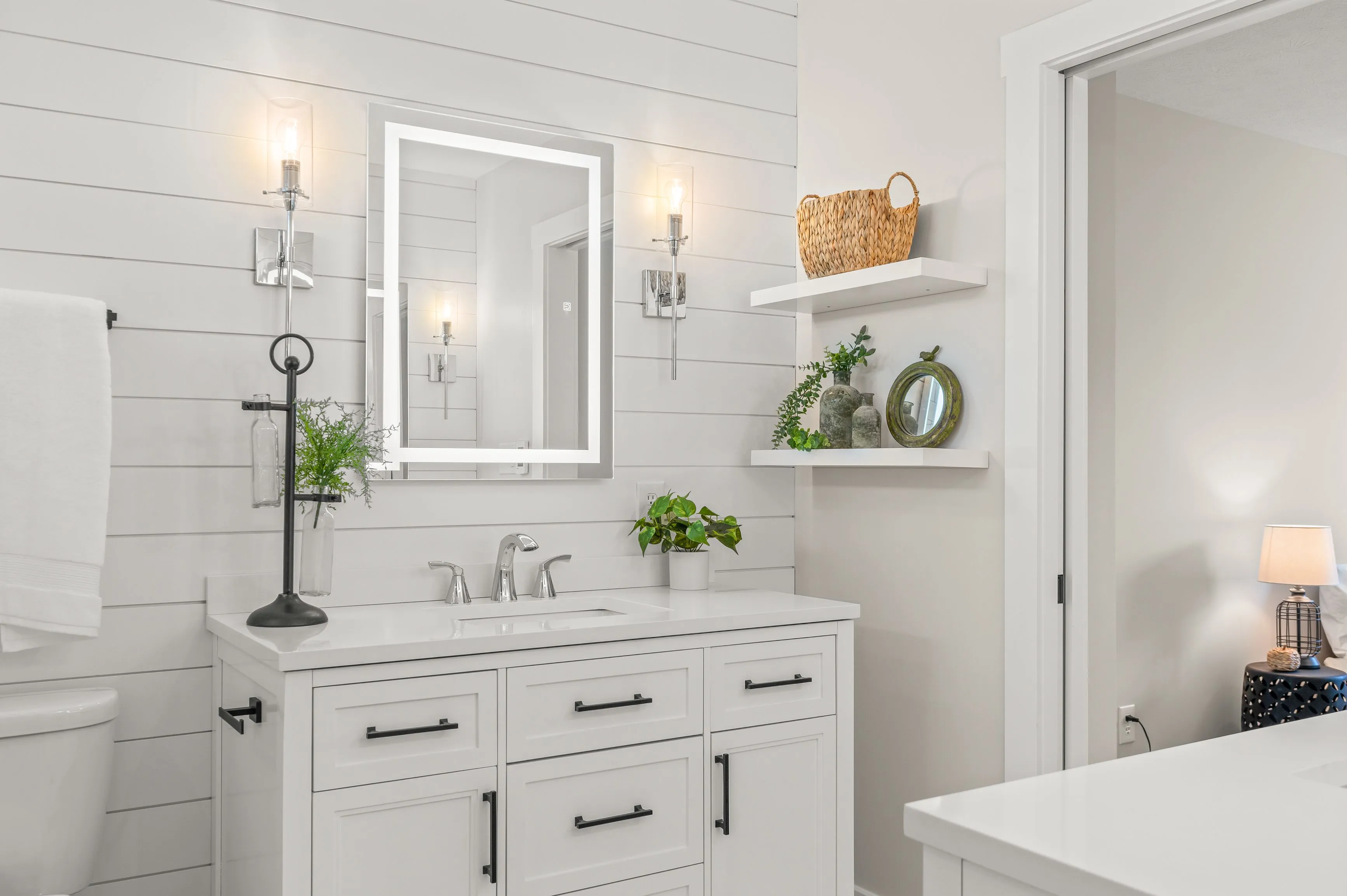 Bright modern bathroom interior with white vanity, mirror, and decorative plants.