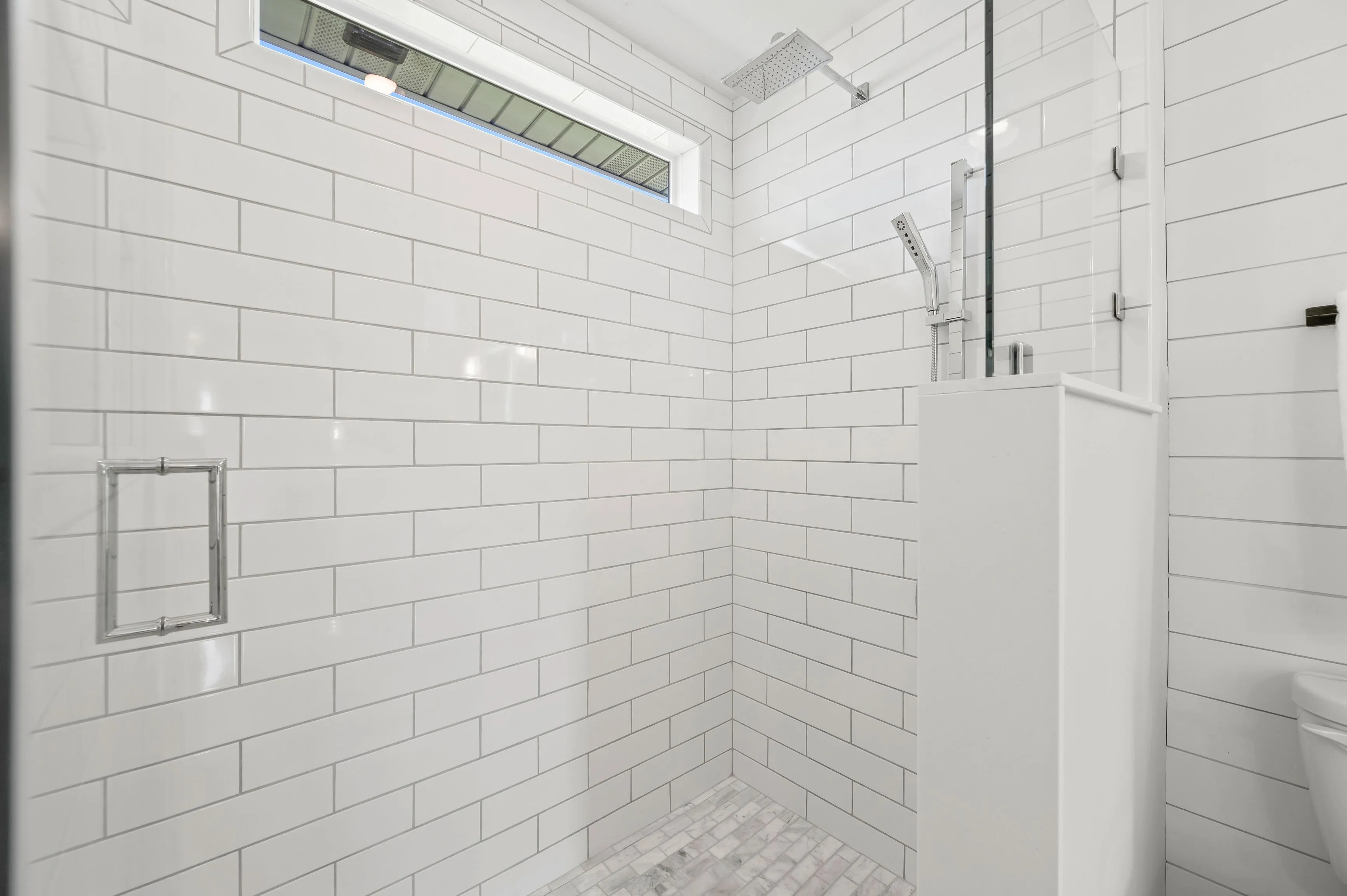 Modern bathroom with white subway tiles, glass shower door, and built-in niche for toiletries.