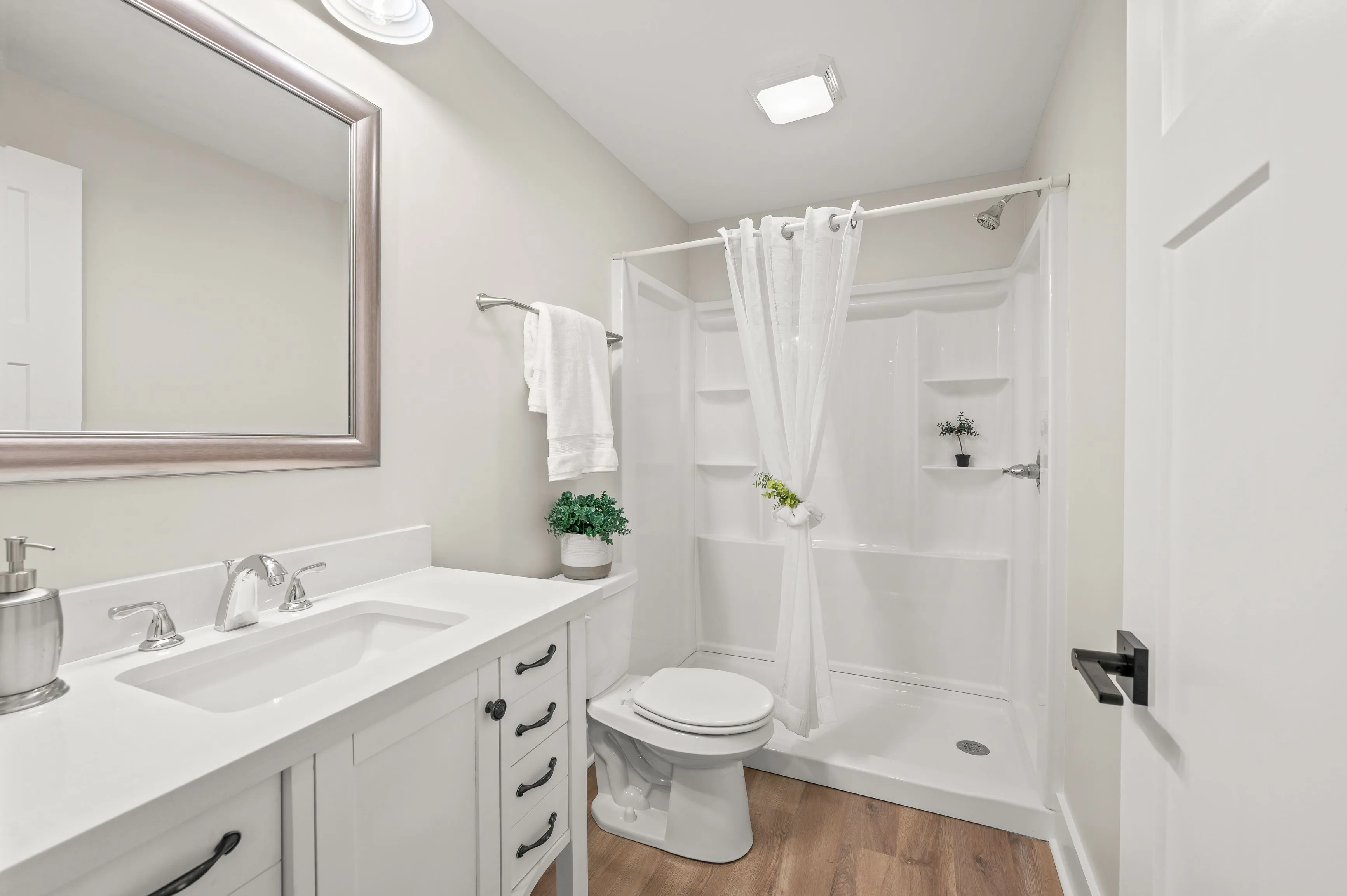 Modern bathroom interior with white vanity cabinet, large mirror, toilet, and shower with white curtain.