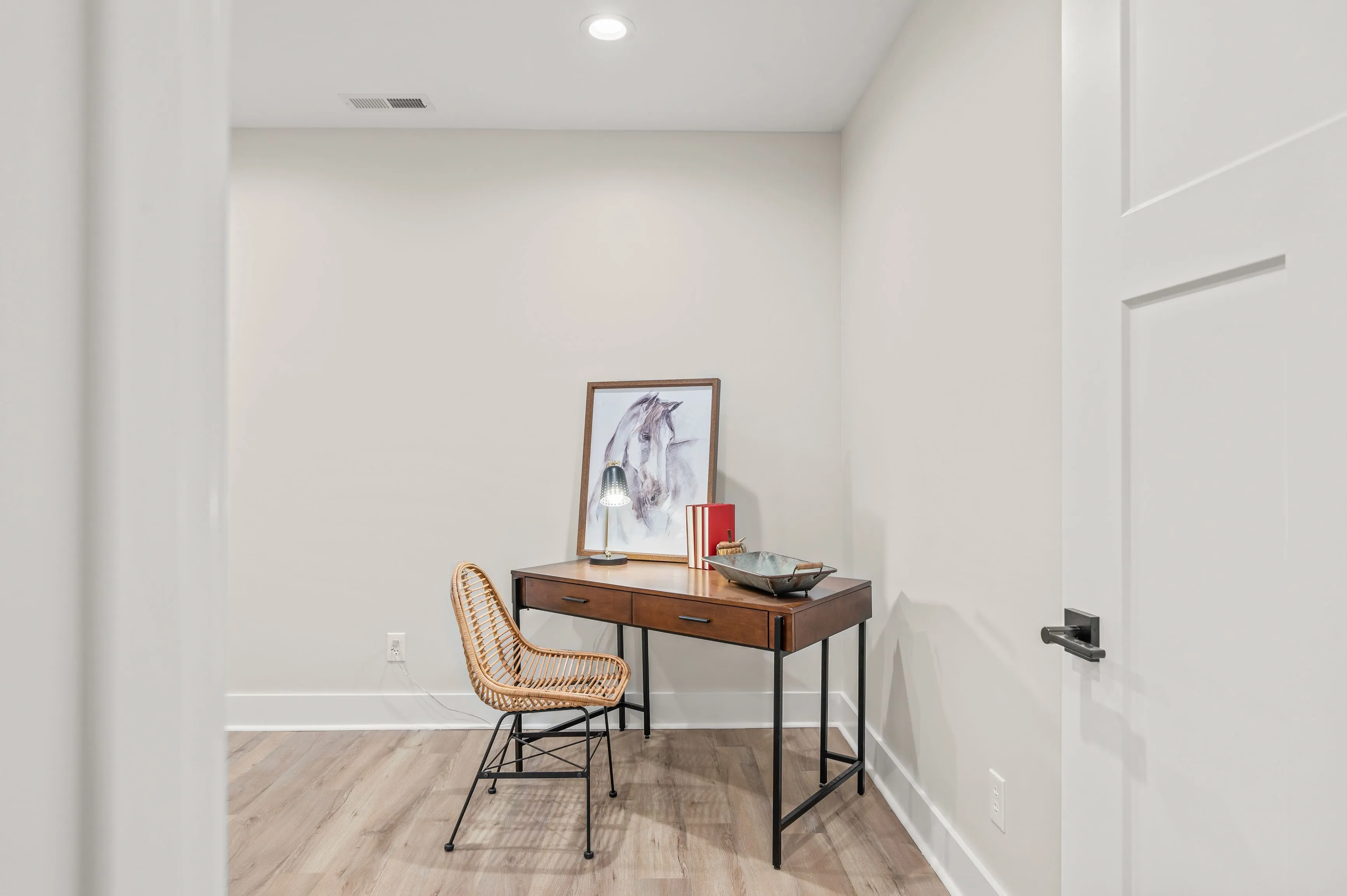 A minimalist home office space with a wooden desk, a framed picture on it, and a chair against a white wall.