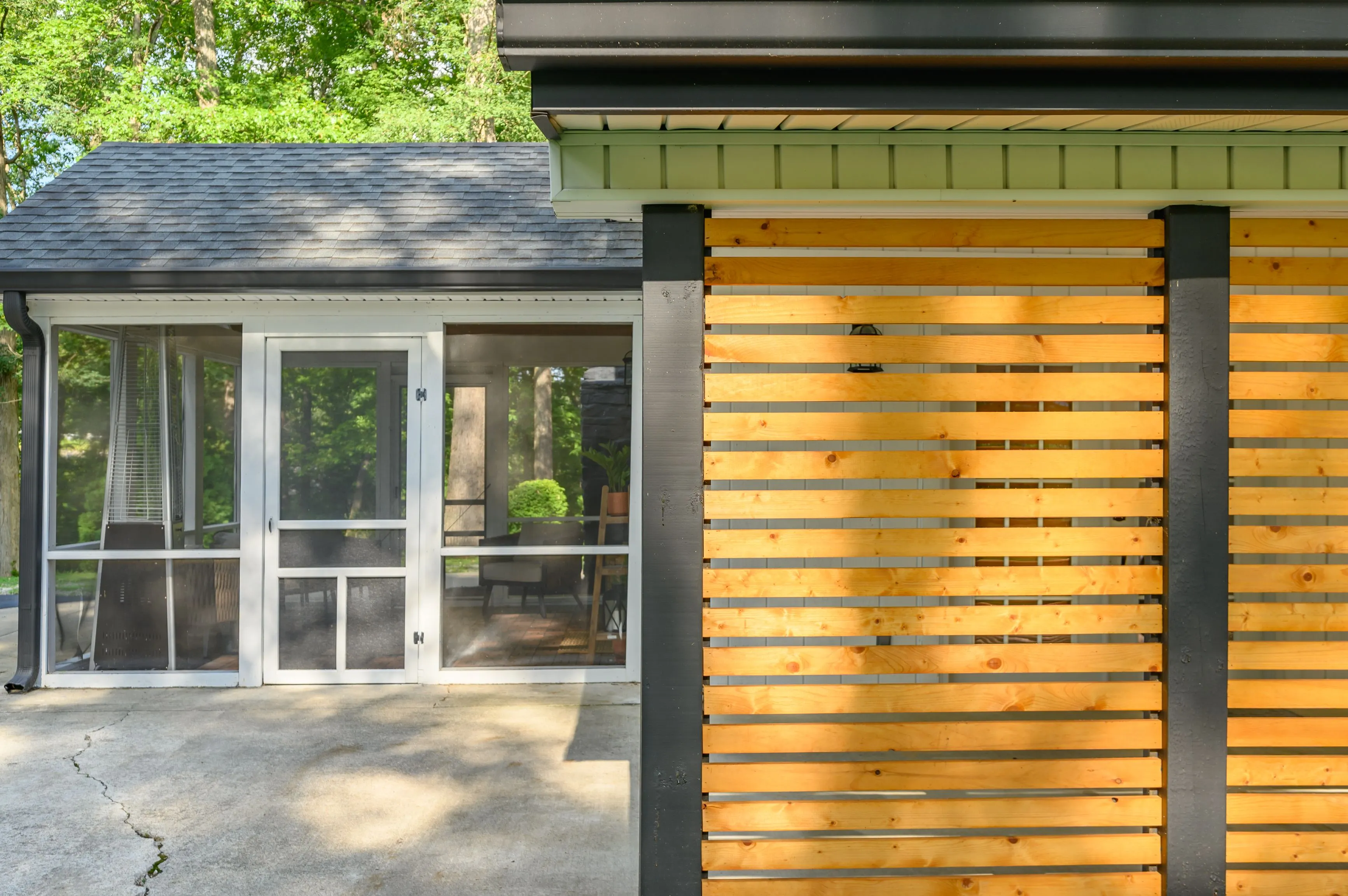Exterior view of a modern house with a wooden slat wall, black support columns, and sliding glass doors leading to a patio.