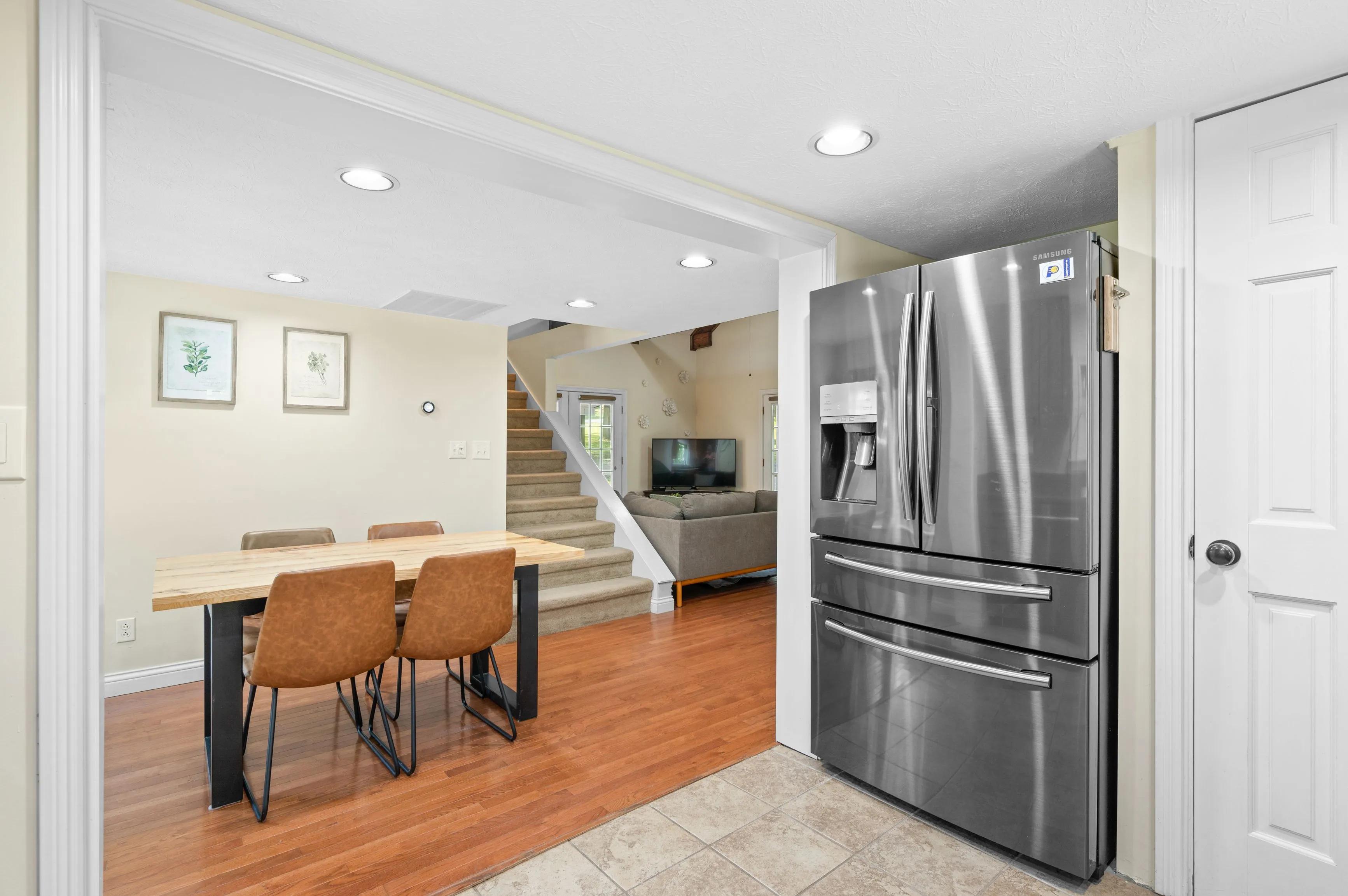 Modern kitchen interior with stainless steel refrigerator, dining table, and staircase in the background.