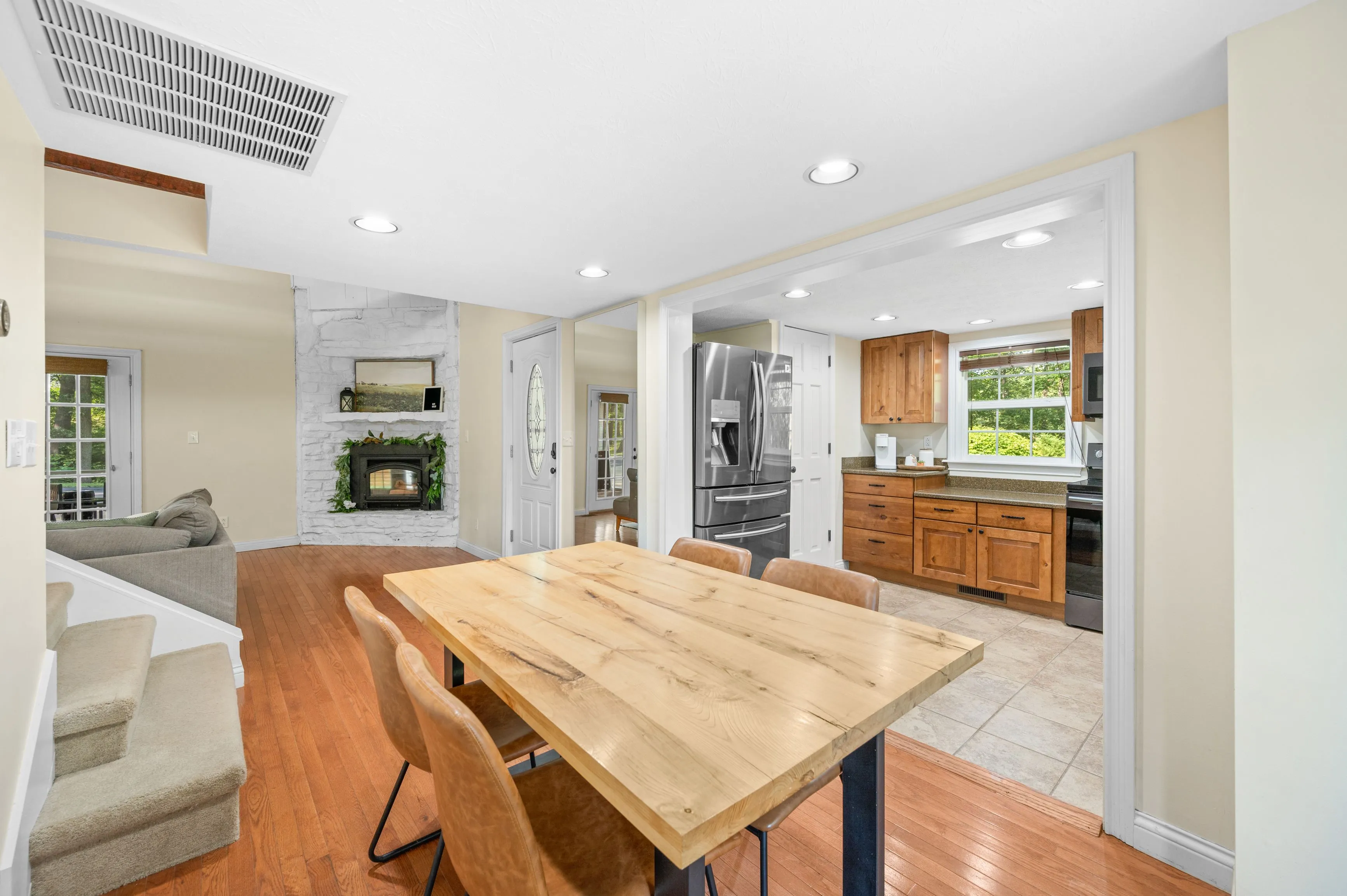 Bright open-plan kitchen and dining area with wooden table, hardwood floors, and white cabinetry.