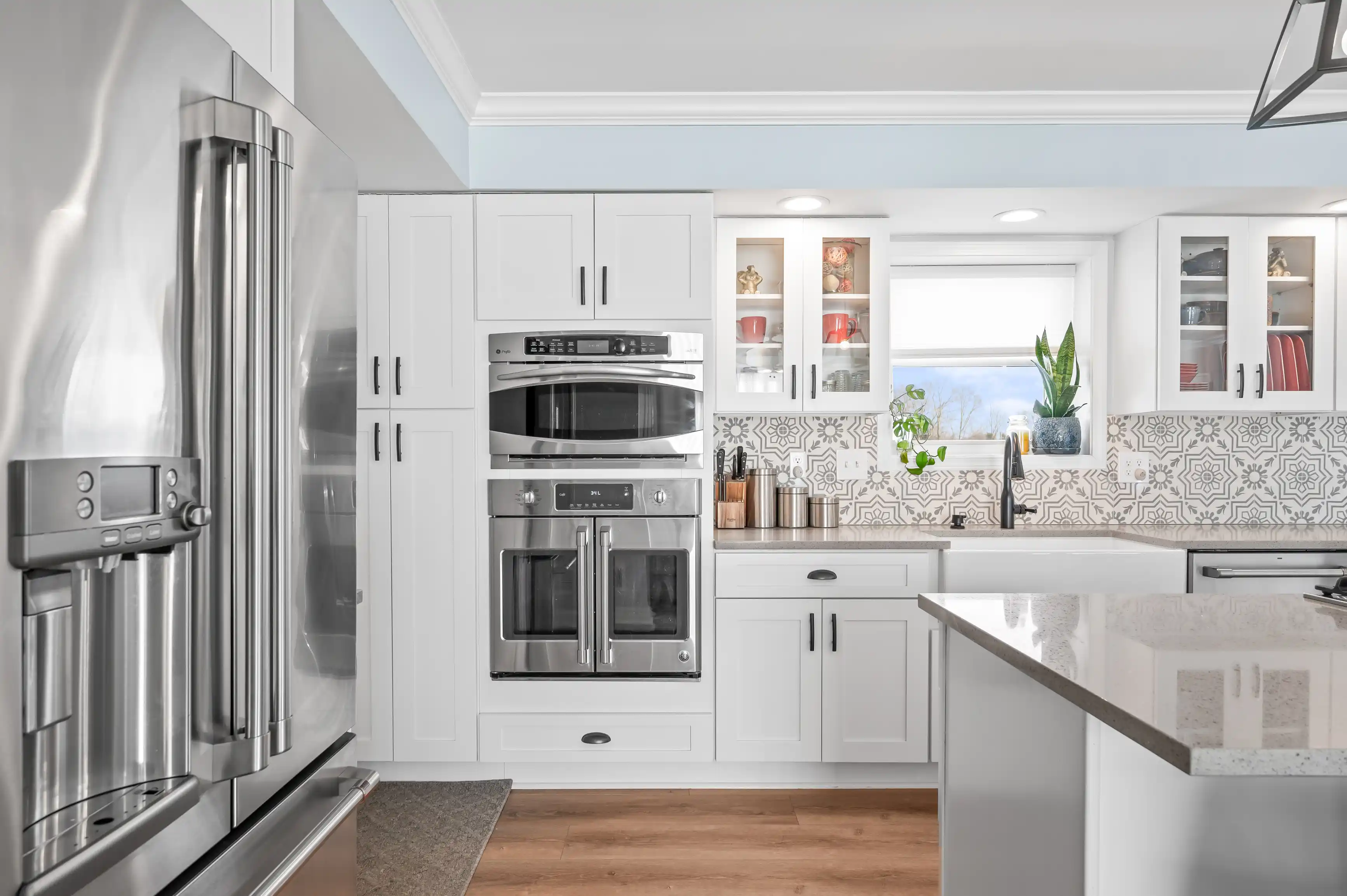 Modern kitchen interior with white cabinets, stainless steel appliances, patterned backsplash, and hardwood flooring.