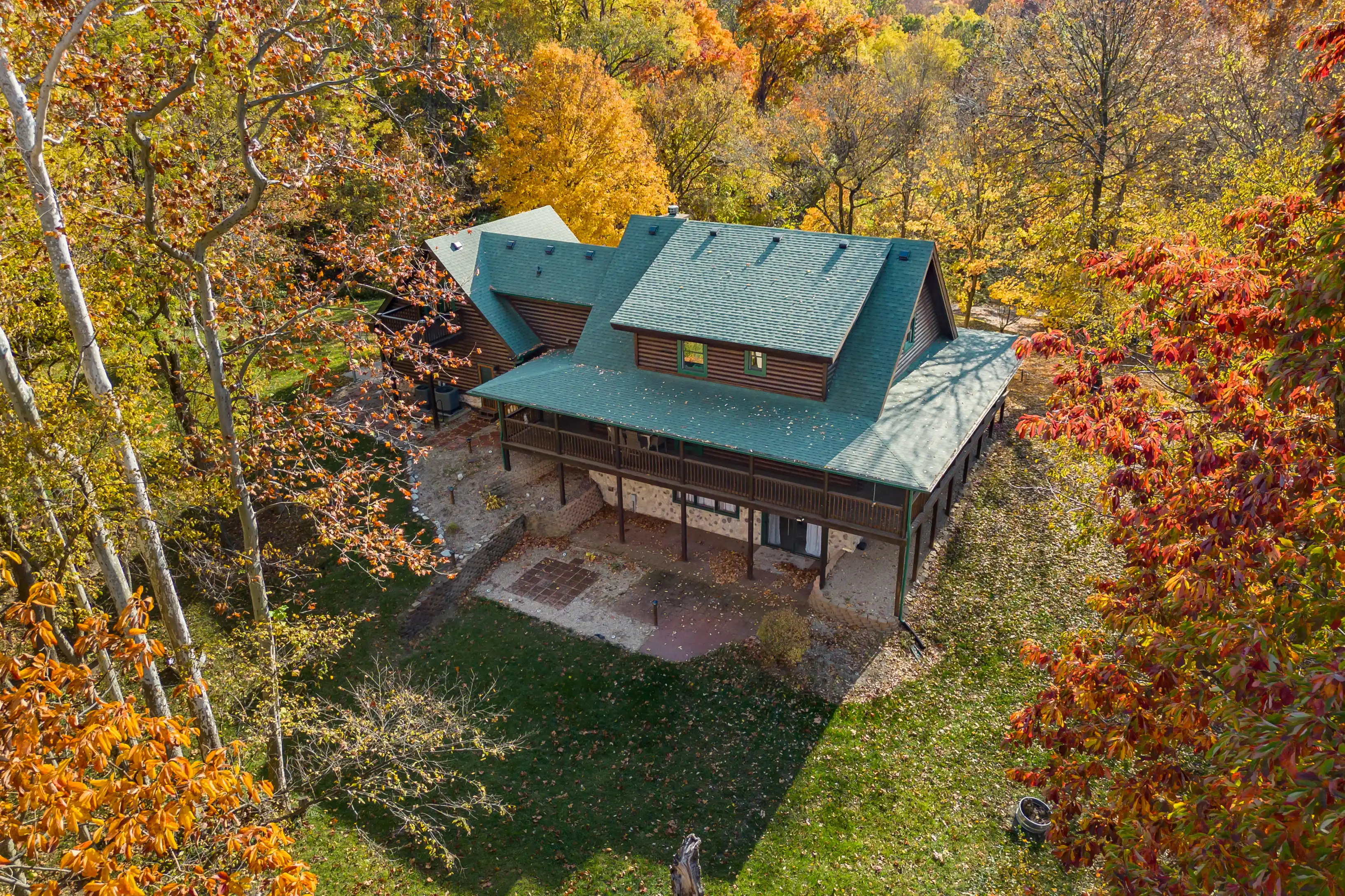 Aerial view of a large cabin with a green roof surrounded by trees with autumn foliage.