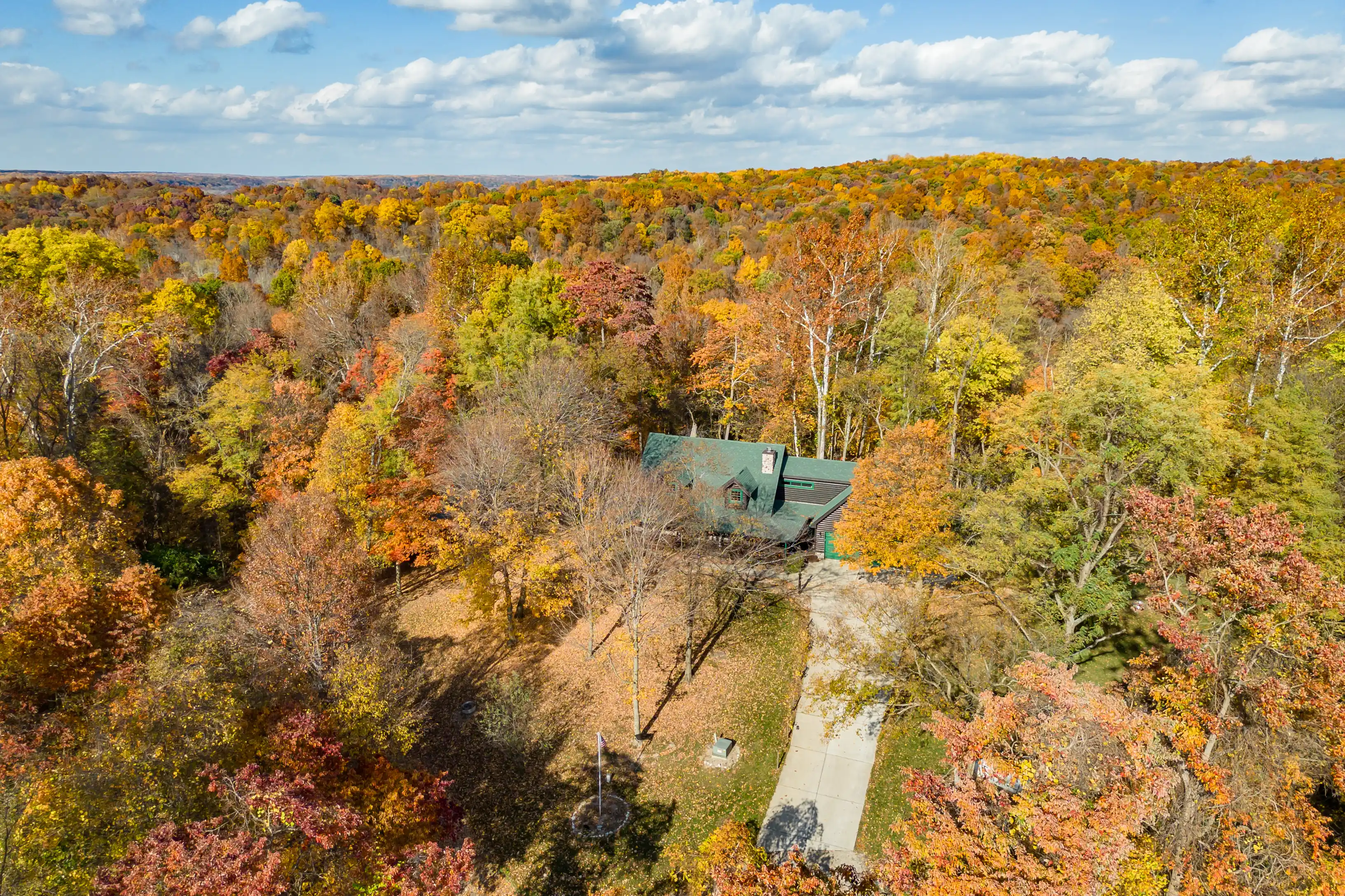 Aerial view of a forest in autumn with a variety of colorful trees and a cabin nestled among them.