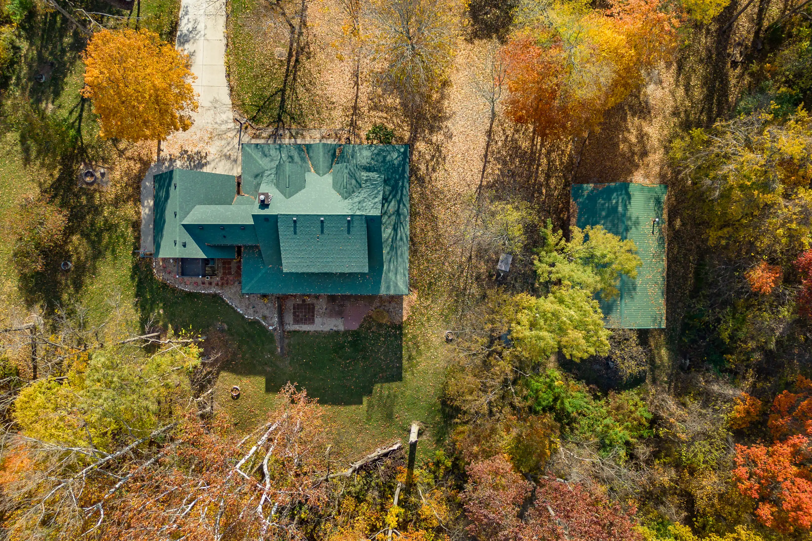 Aerial view of two houses with green roofs surrounded by trees with autumn foliage.