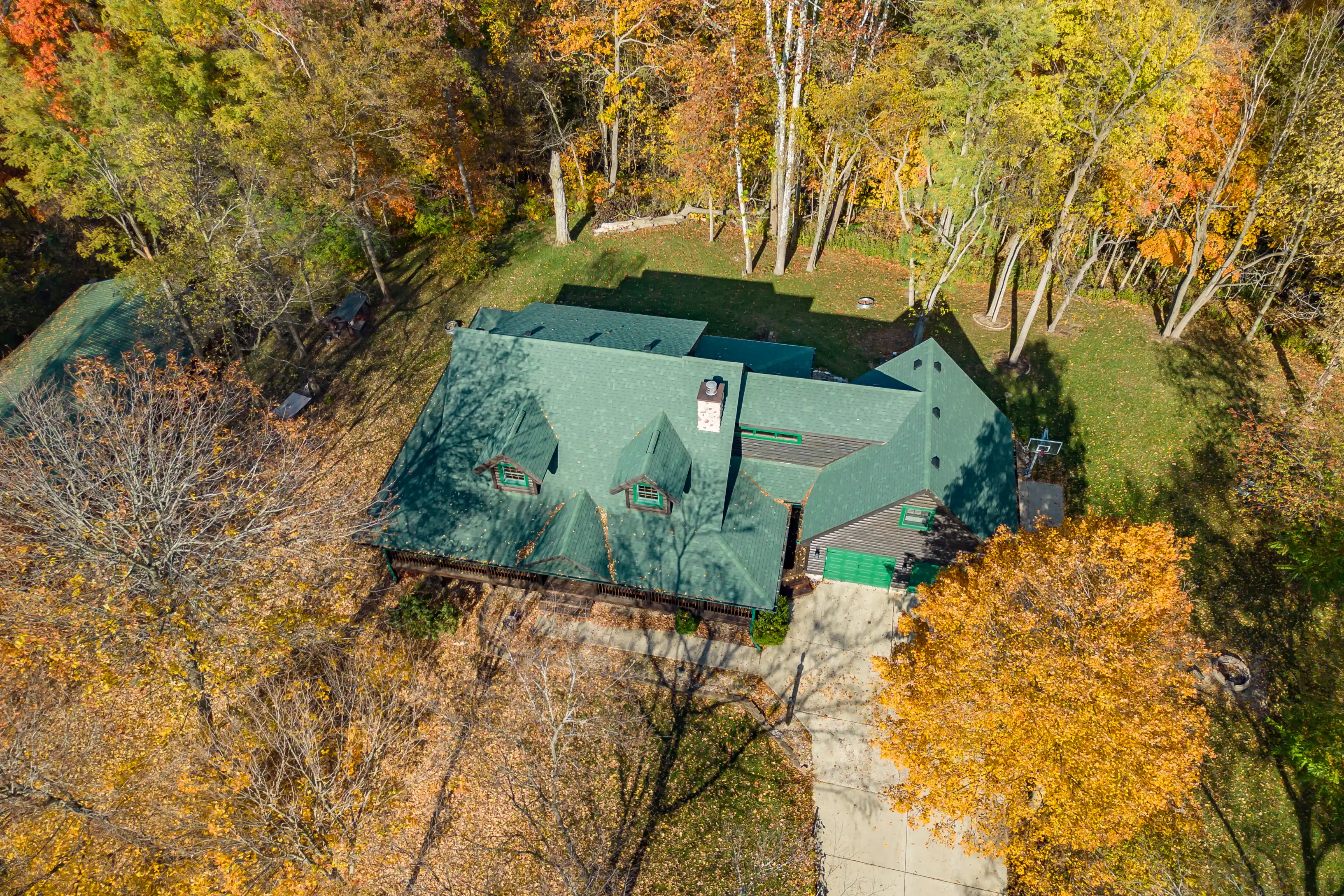 Aerial view of a large house with a green roof surrounded by trees in autumn foliage.