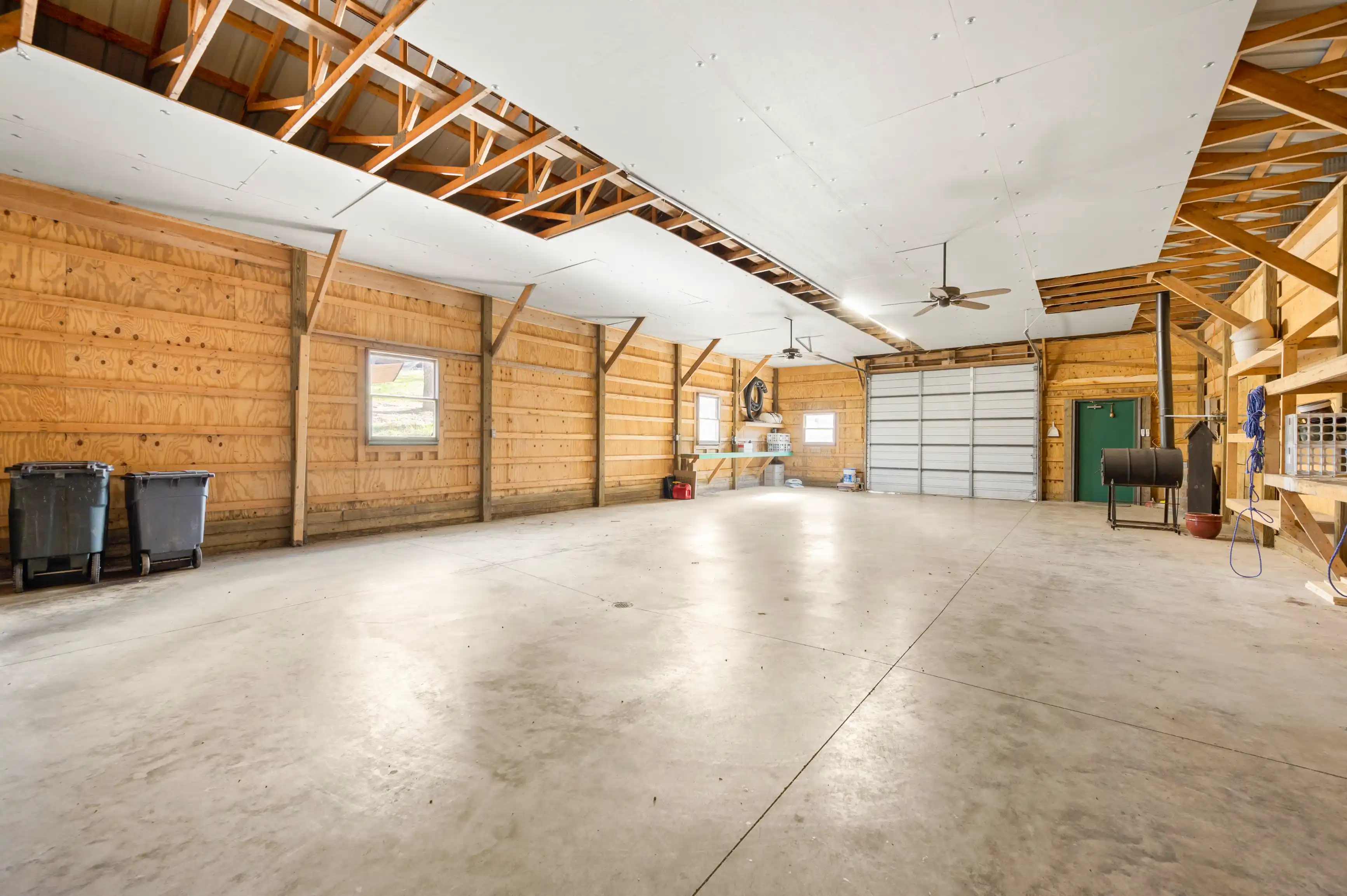 Spacious empty garage interior with wooden walls, concrete floor, and an open ceiling showing rafters.
