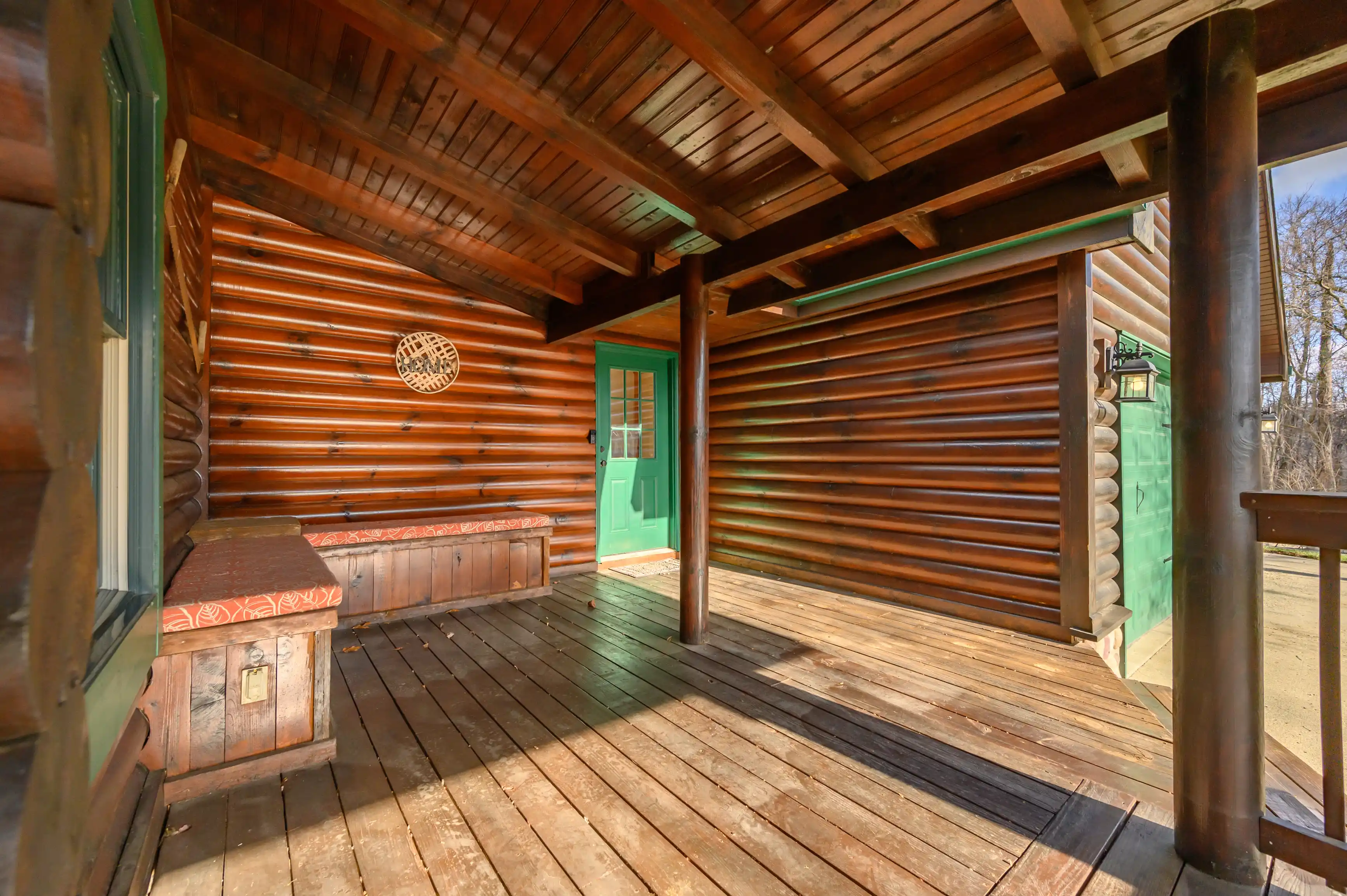 Spacious wooden porch of a log cabin with a bright green door, decorated bench, and intricate carved details along the exterior walls.