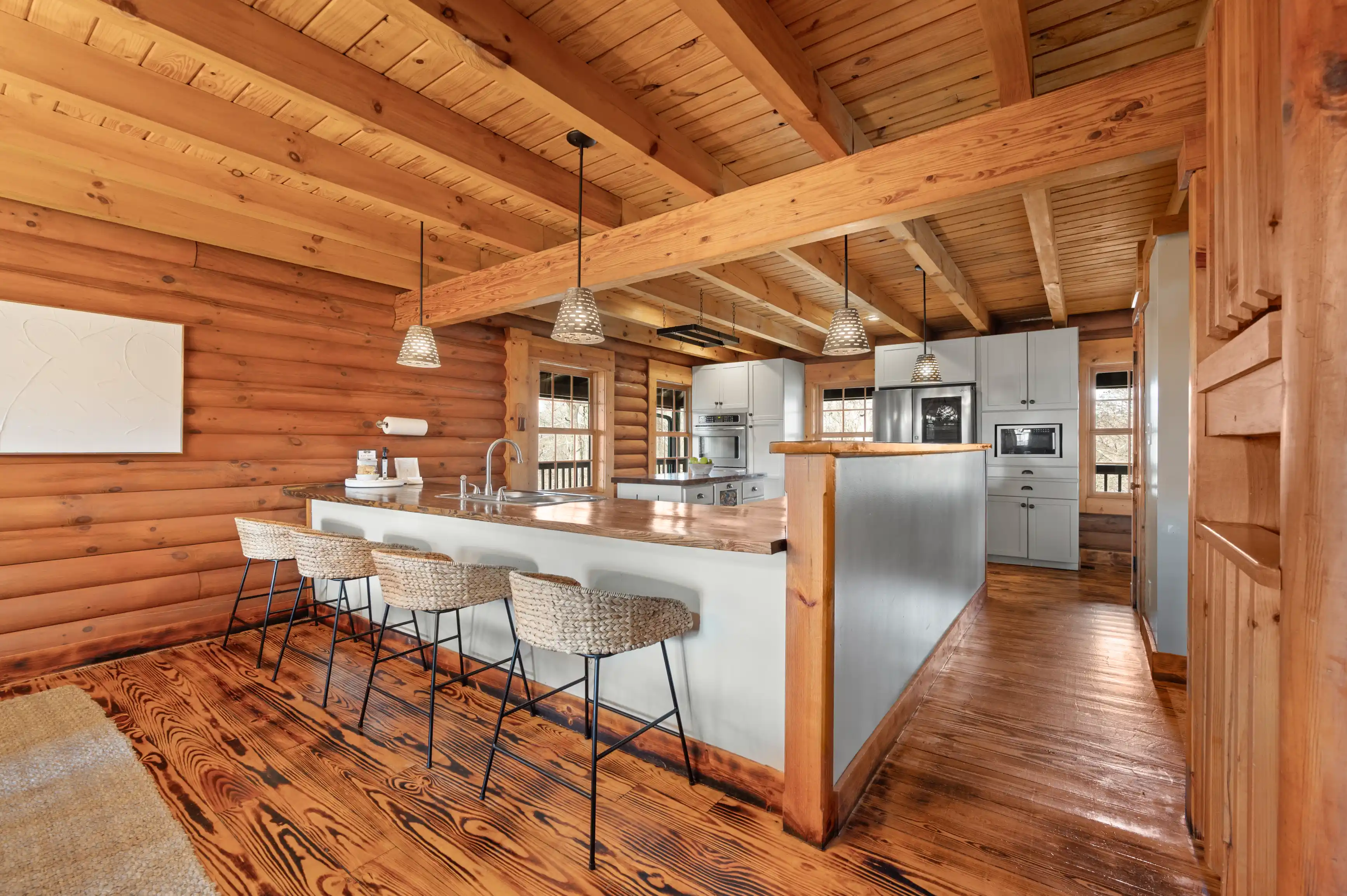Rustic log cabin interior kitchen with wood beams, stainless steel appliances, and a bar seating area.