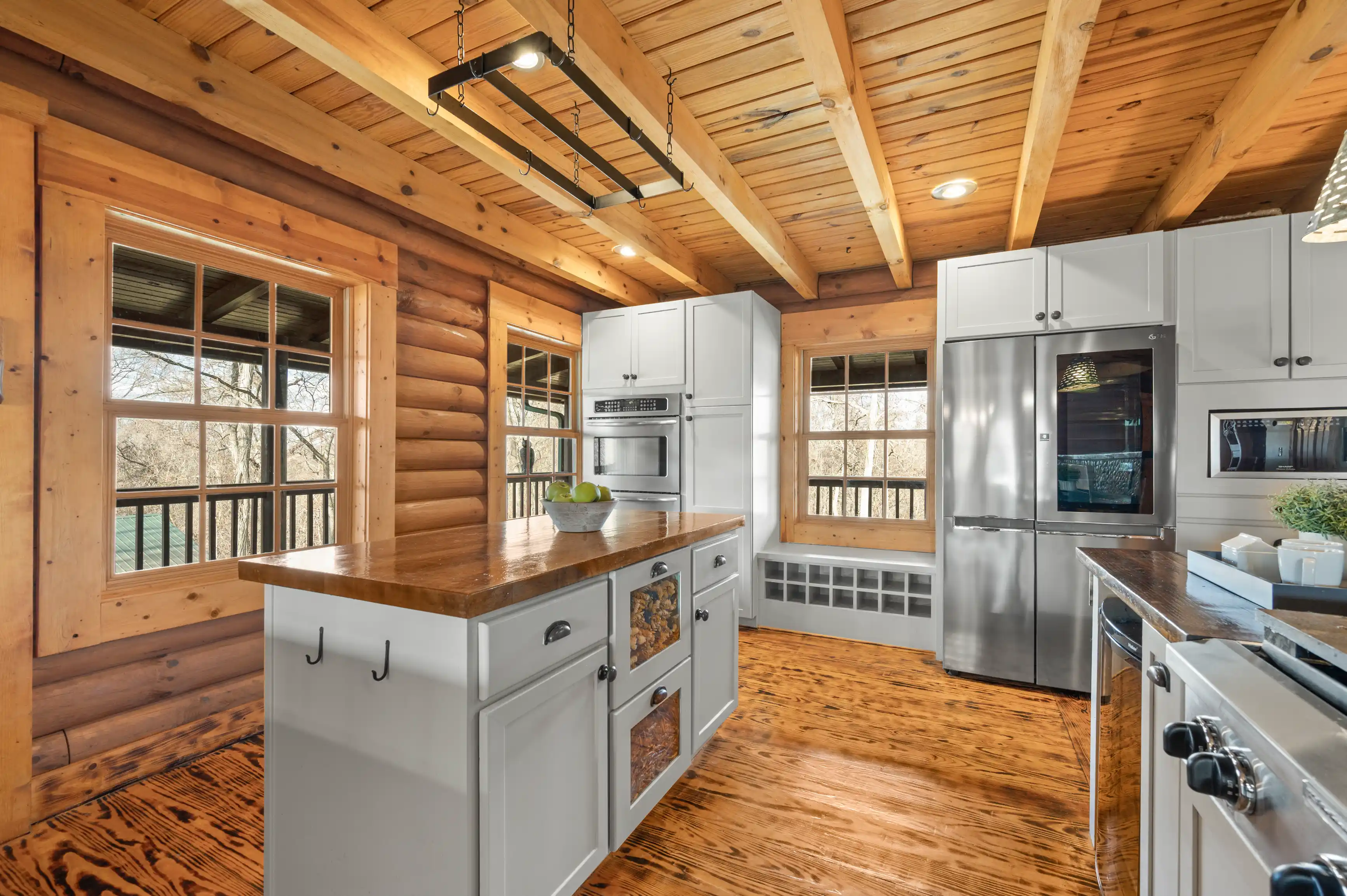 Rustic log cabin kitchen interior with modern appliances, wooden countertops, and hanging industrial light fixture.