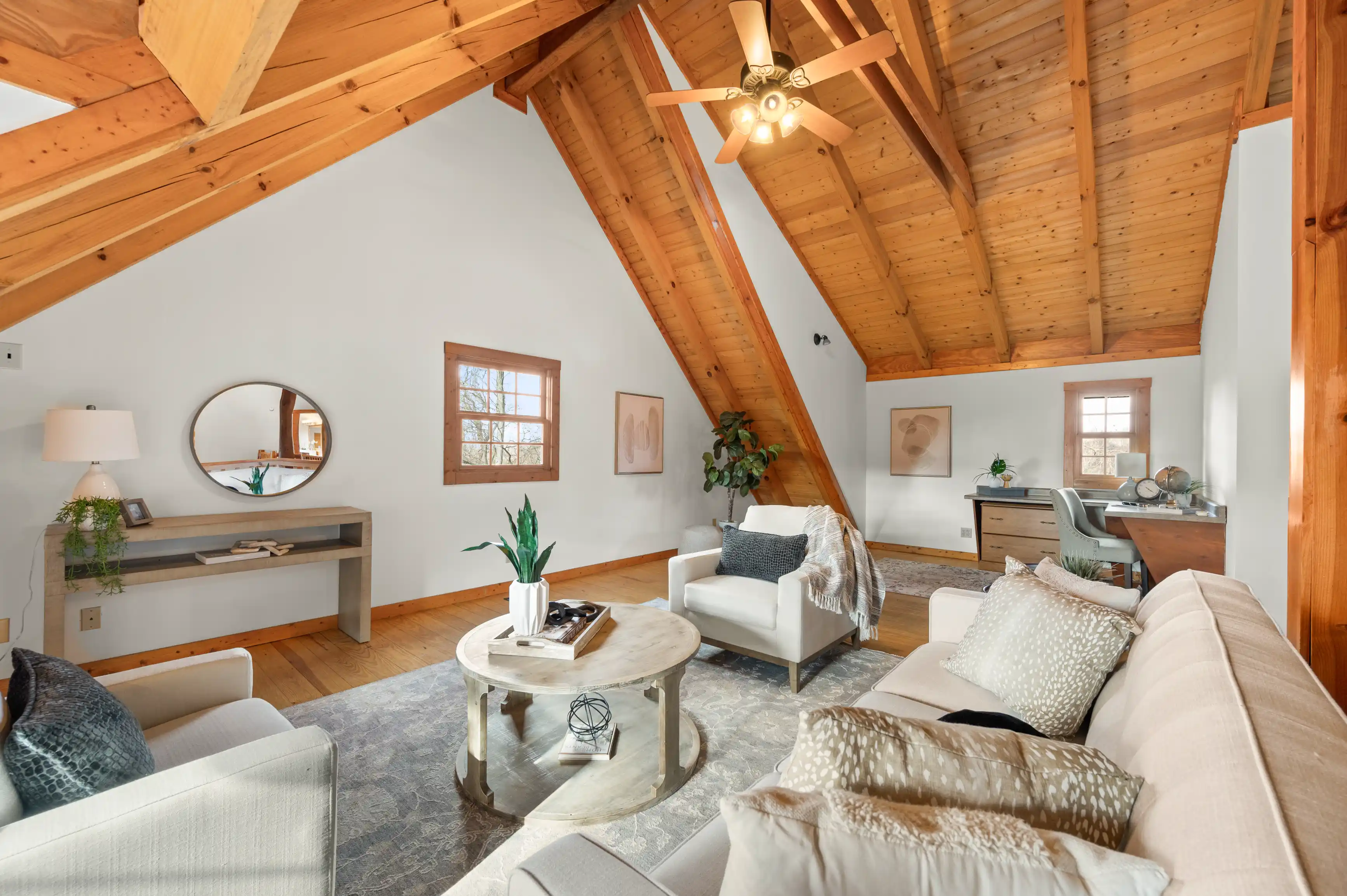Spacious living room in a cabin with vaulted ceilings, exposed beams, hardwood floors, and a mix of modern and rustic decor.